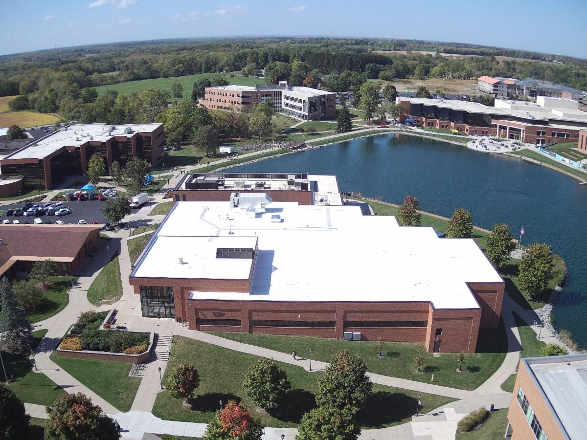 Aerial view of a campus with brick buildings, walkways, and a large pond surrounded by trees.