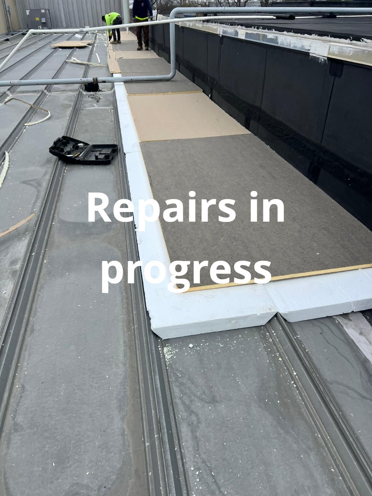 Rooftop repairs in progress beside raised white edging and black roofing material