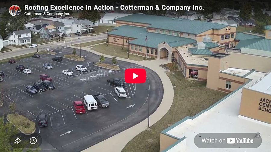 Aerial view of a parking lot beside a beige building and construction site with a red play button overlay