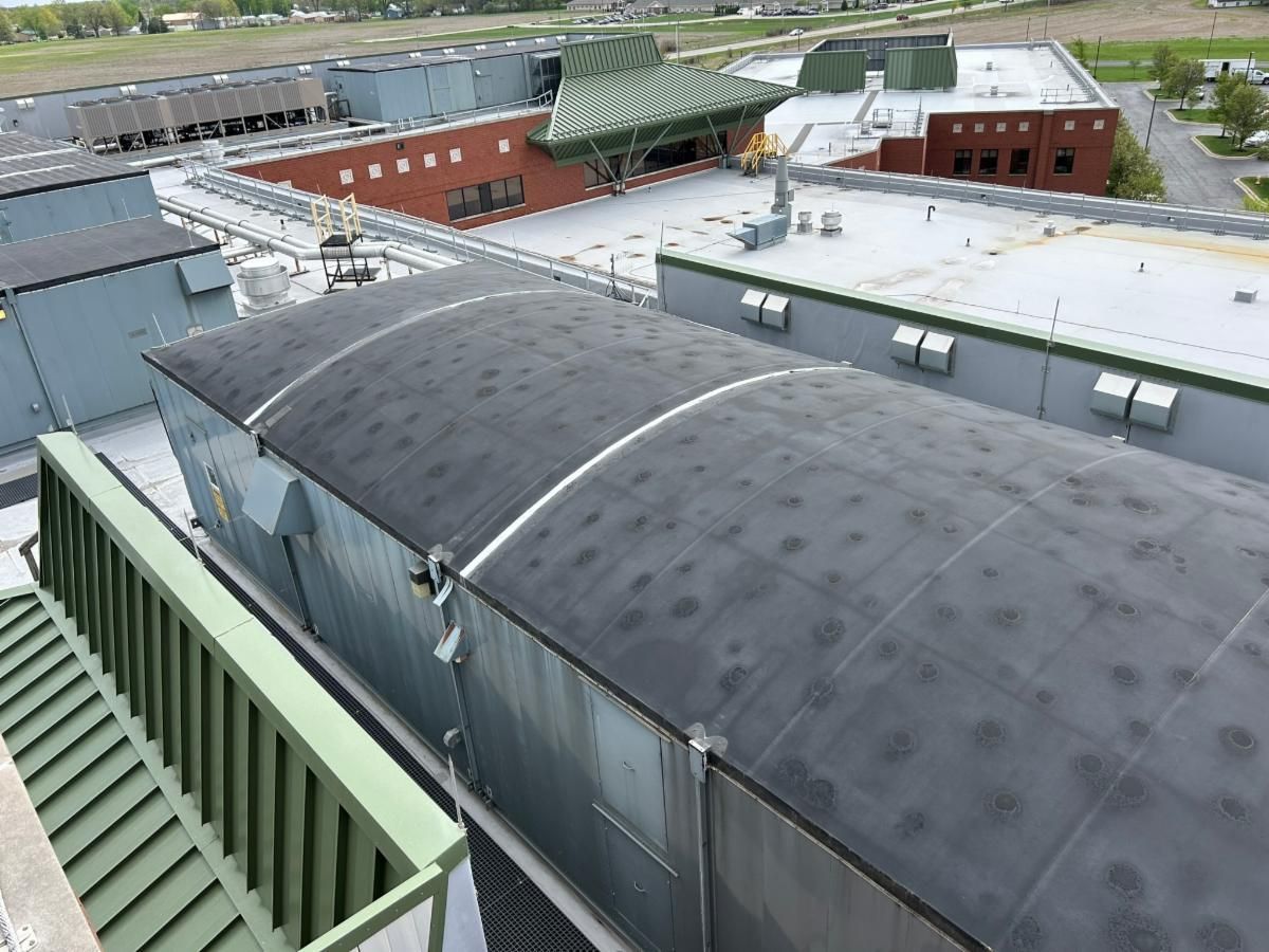 Overhead view of several industrial building roofs with curved metal sections, some with dark spots.