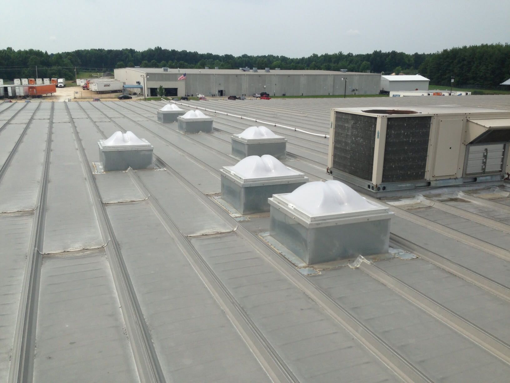 Rooftop view of a commercial building with skylights and HVAC units; metal roof.
