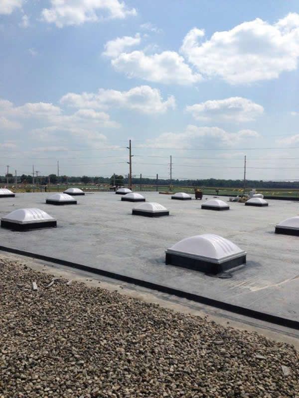 Flat commercial roof with multiple skylights under a partly cloudy sky.