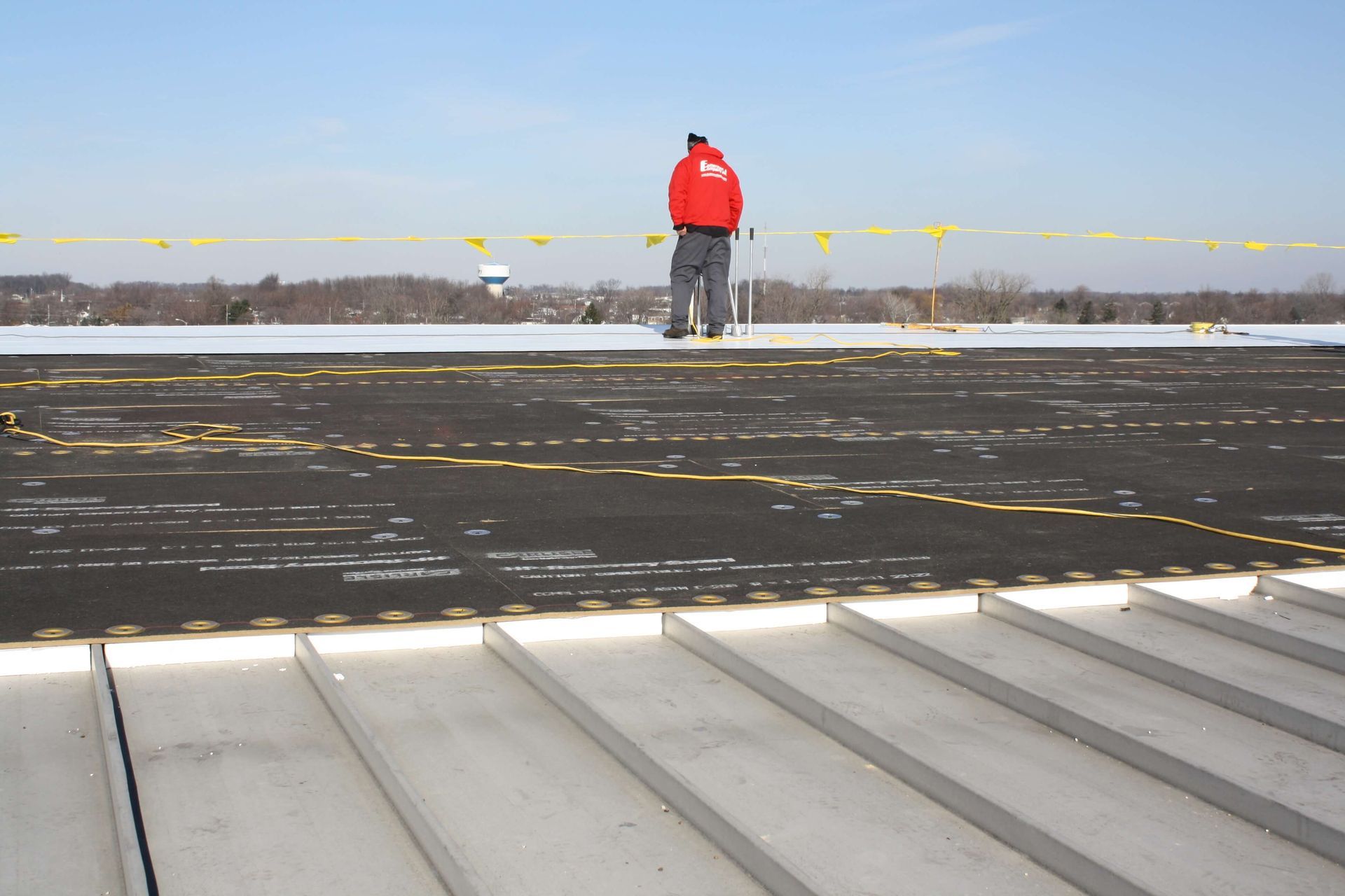 Person in red jacket stands on a snowy rooftop, with yellow safety barriers.