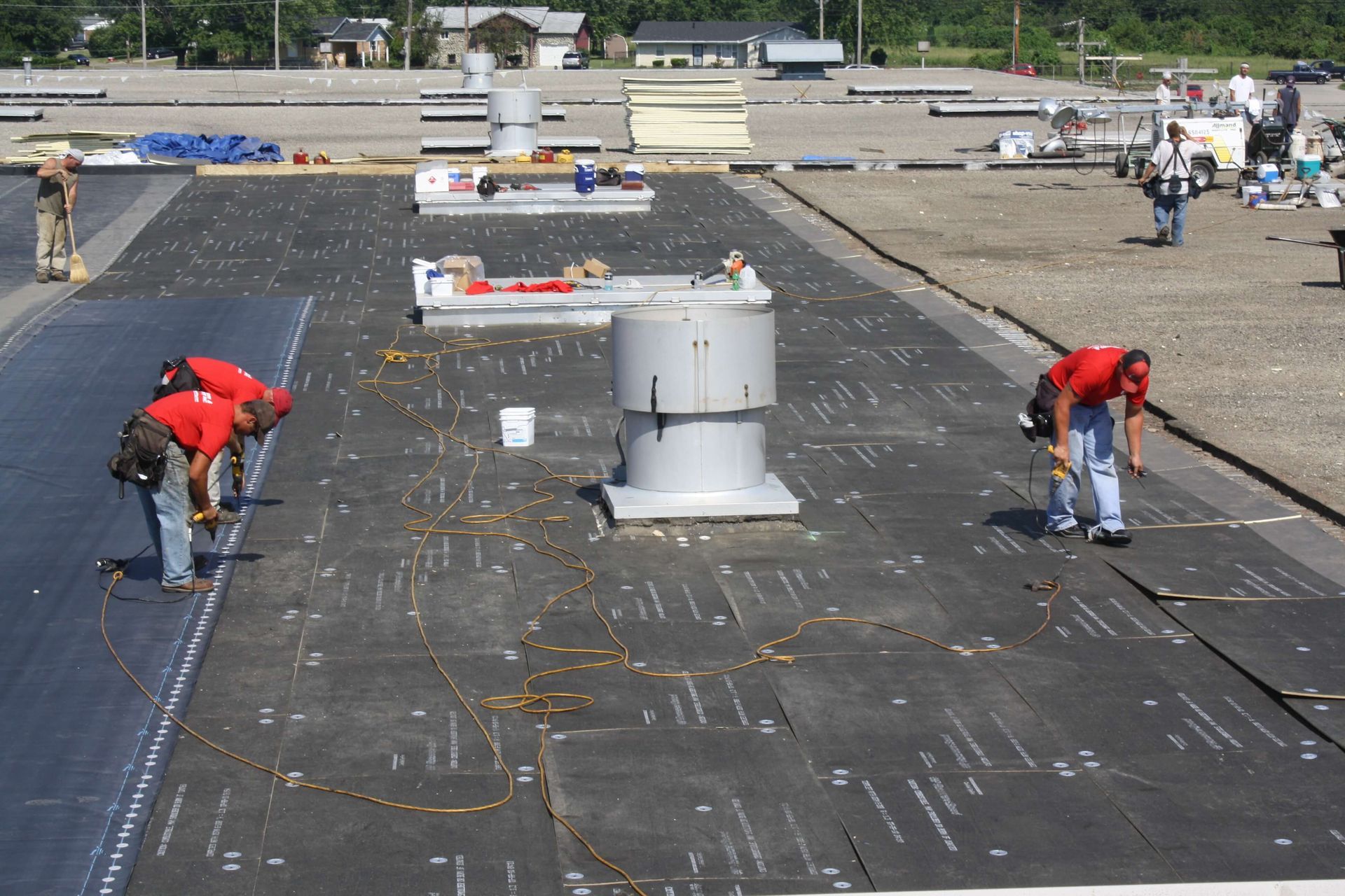 Roofers in red shirts installing roofing material on a large, flat commercial roof.