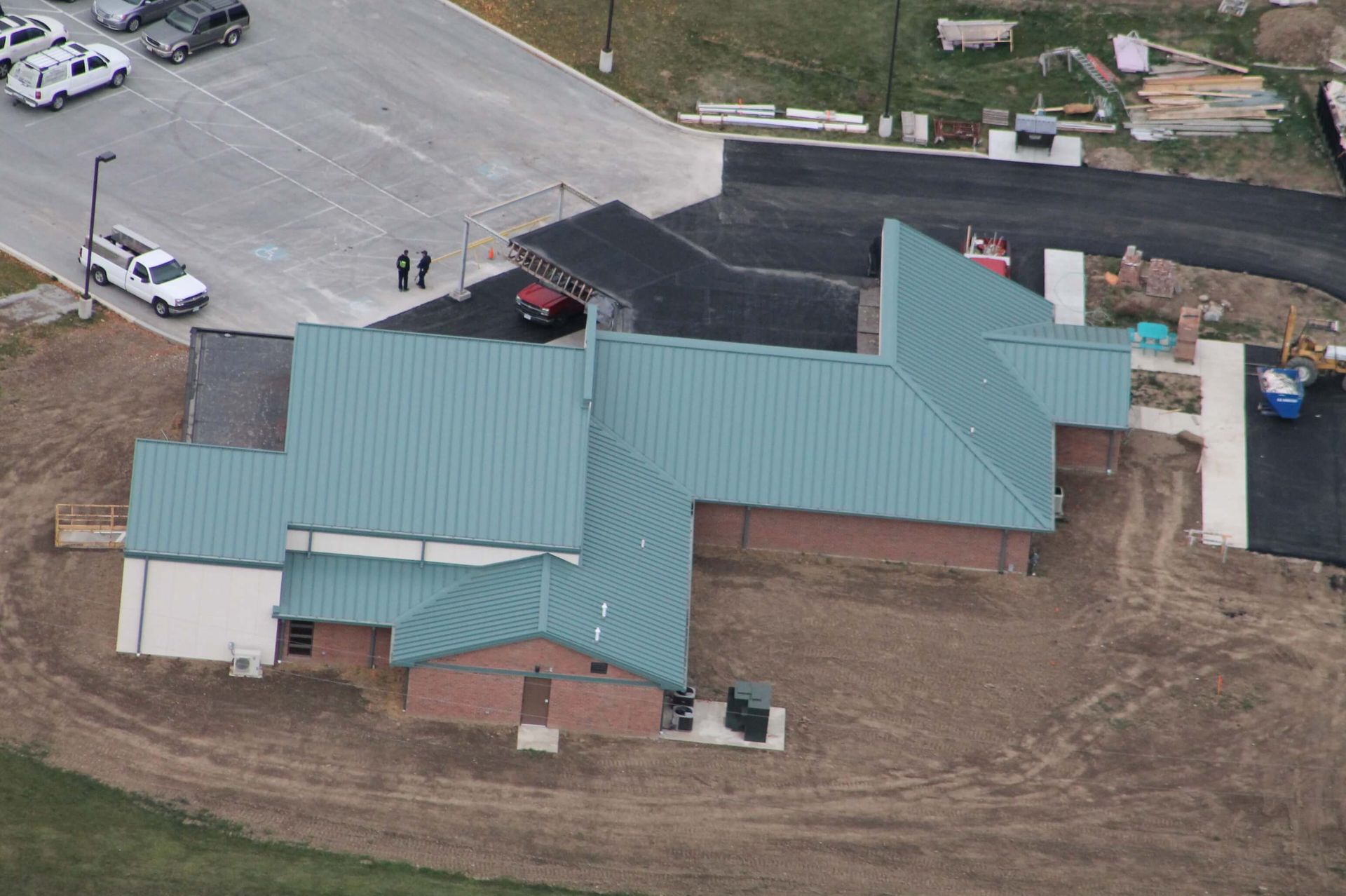 Overhead view of a building with a teal roof and brown brick walls; parking lot with cars visible.