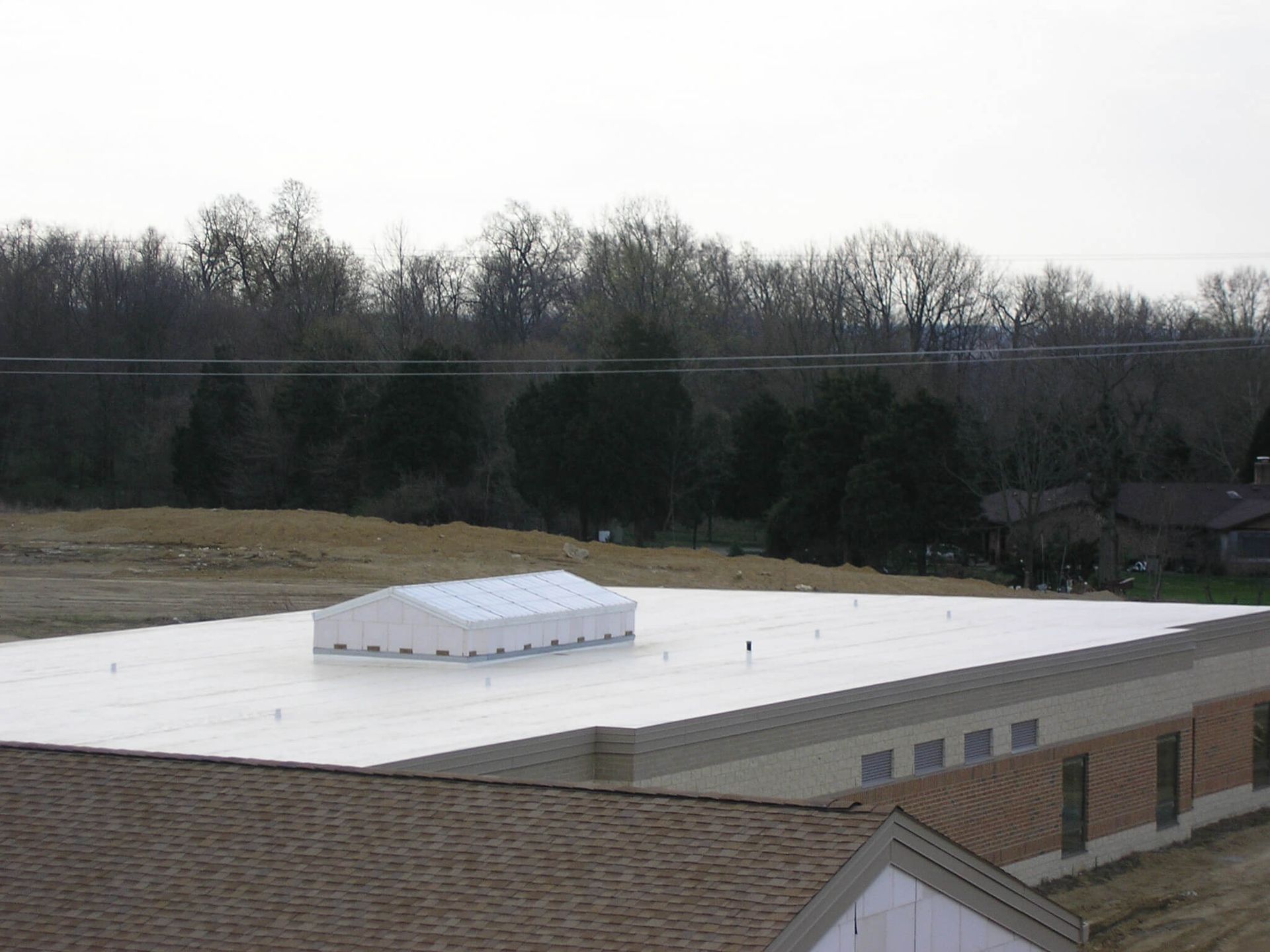 A low-angle view of a large flat roof with a white tent structure on top, trees in the background.