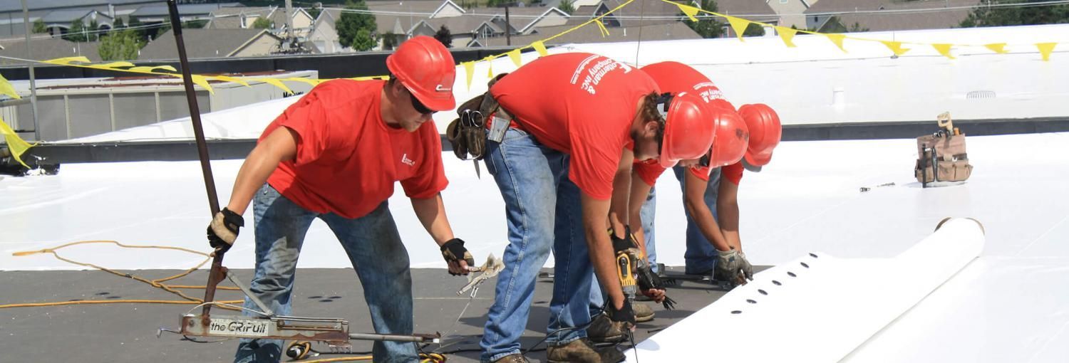 Construction workers in red shirts and hard hats working on a roof, securing something.