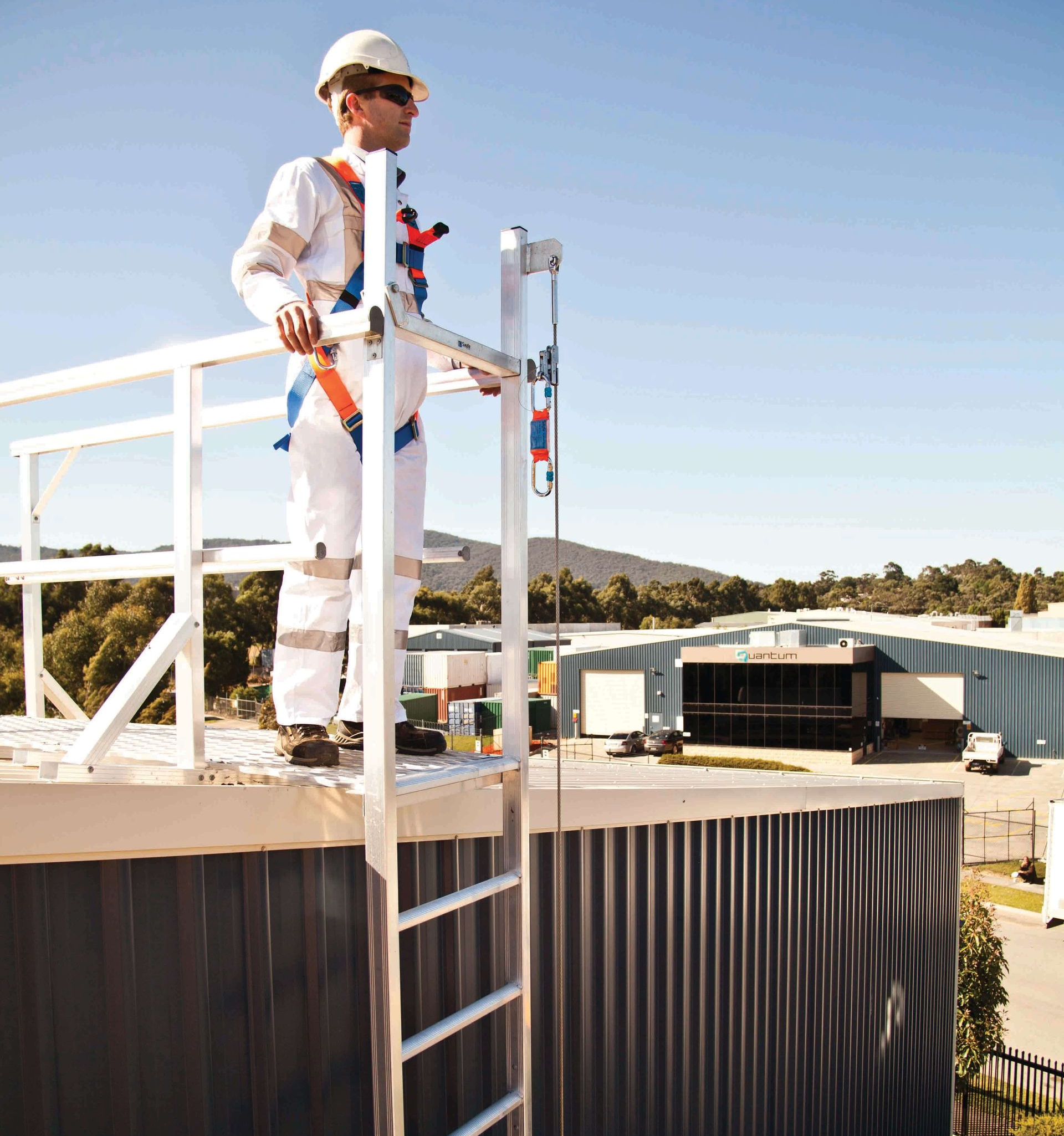 A worker in a safety harness stands on a rooftop platform, looking outward.