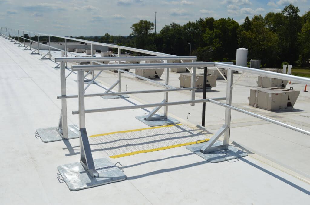 Metal rooftop fall protection system on a white roof, in front of trees.