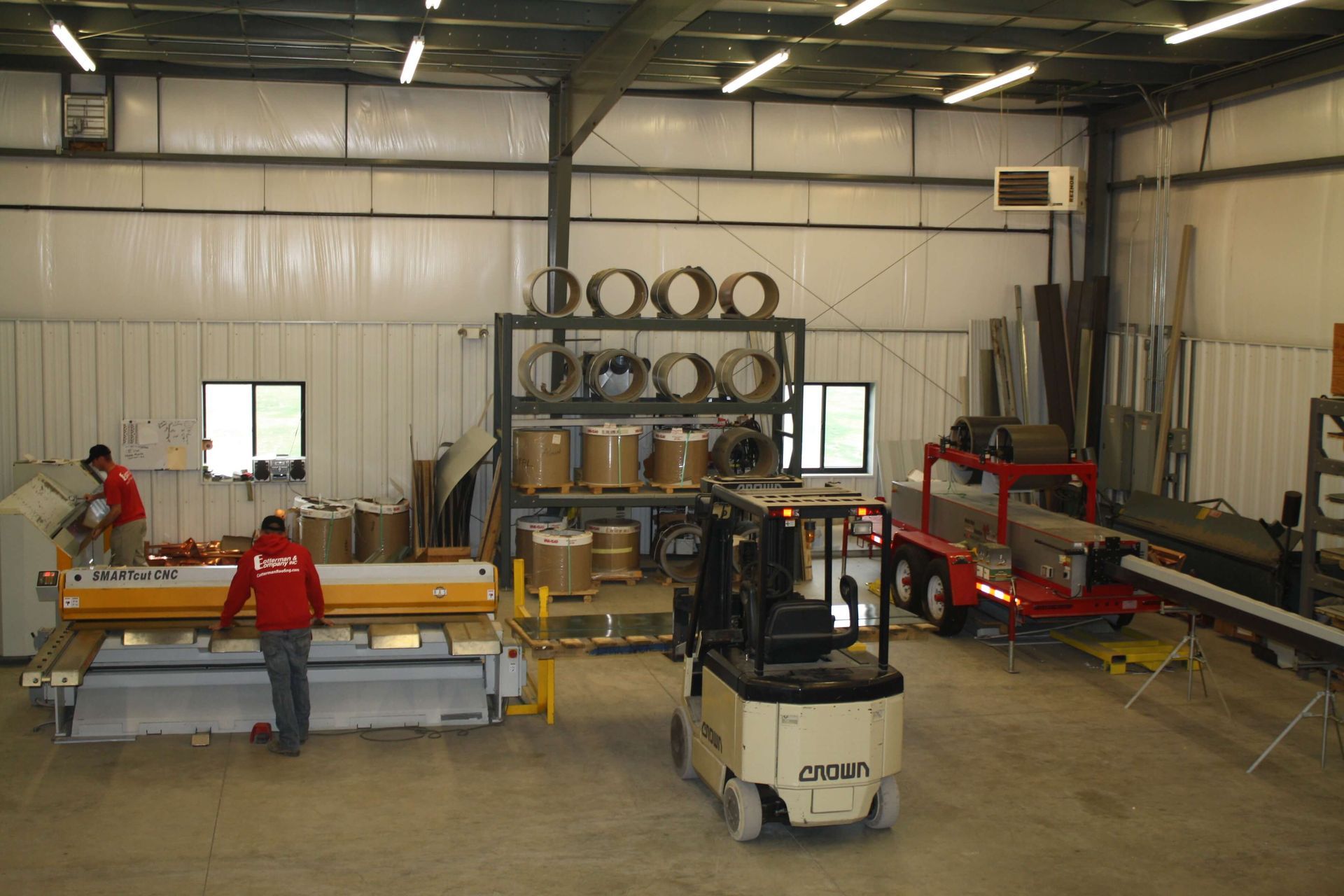 Warehouse interior with workers near machinery and materials. A forklift is in the foreground.