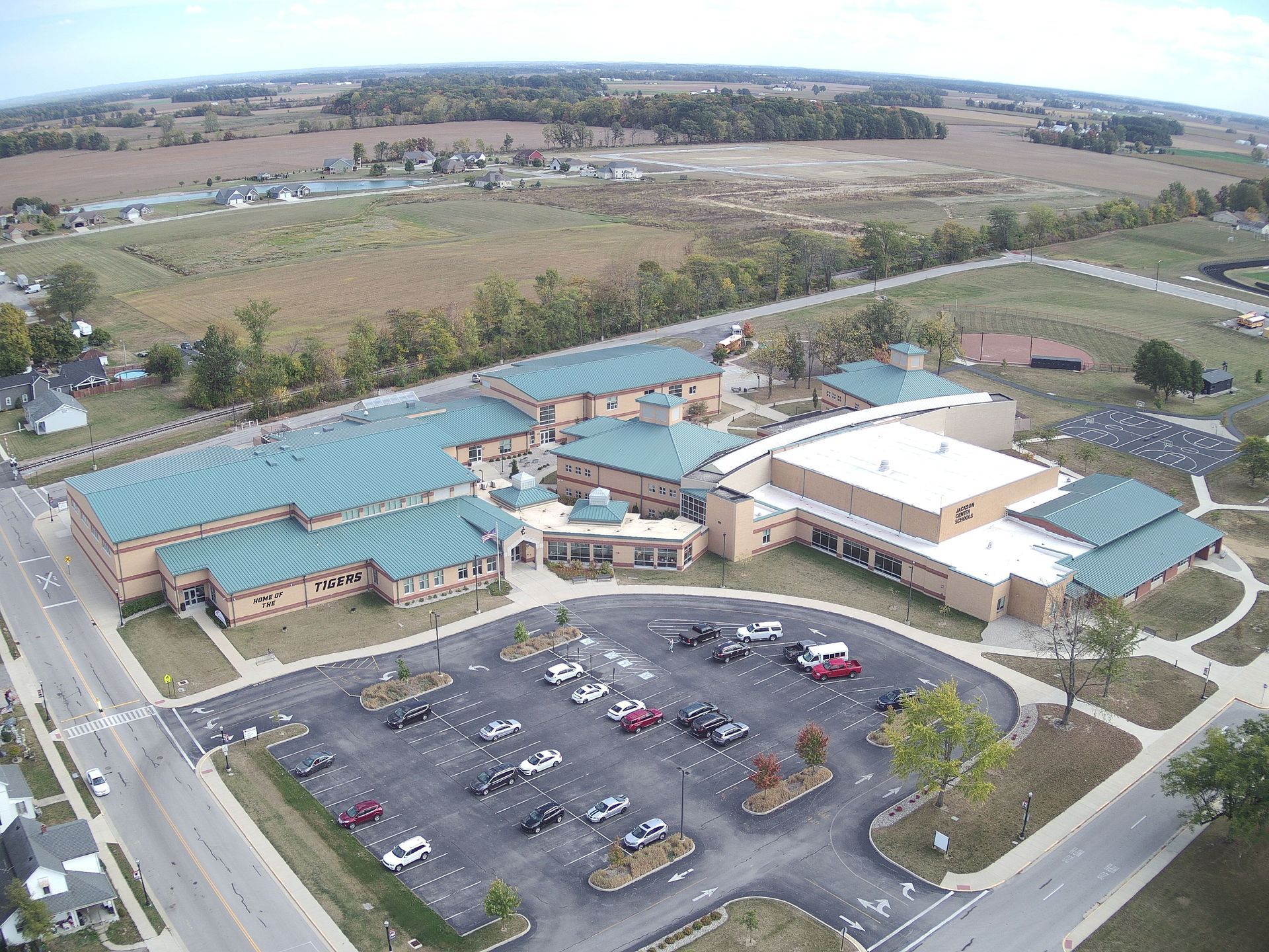 Aerial view of a school building with a parking lot in front, and fields in the background.