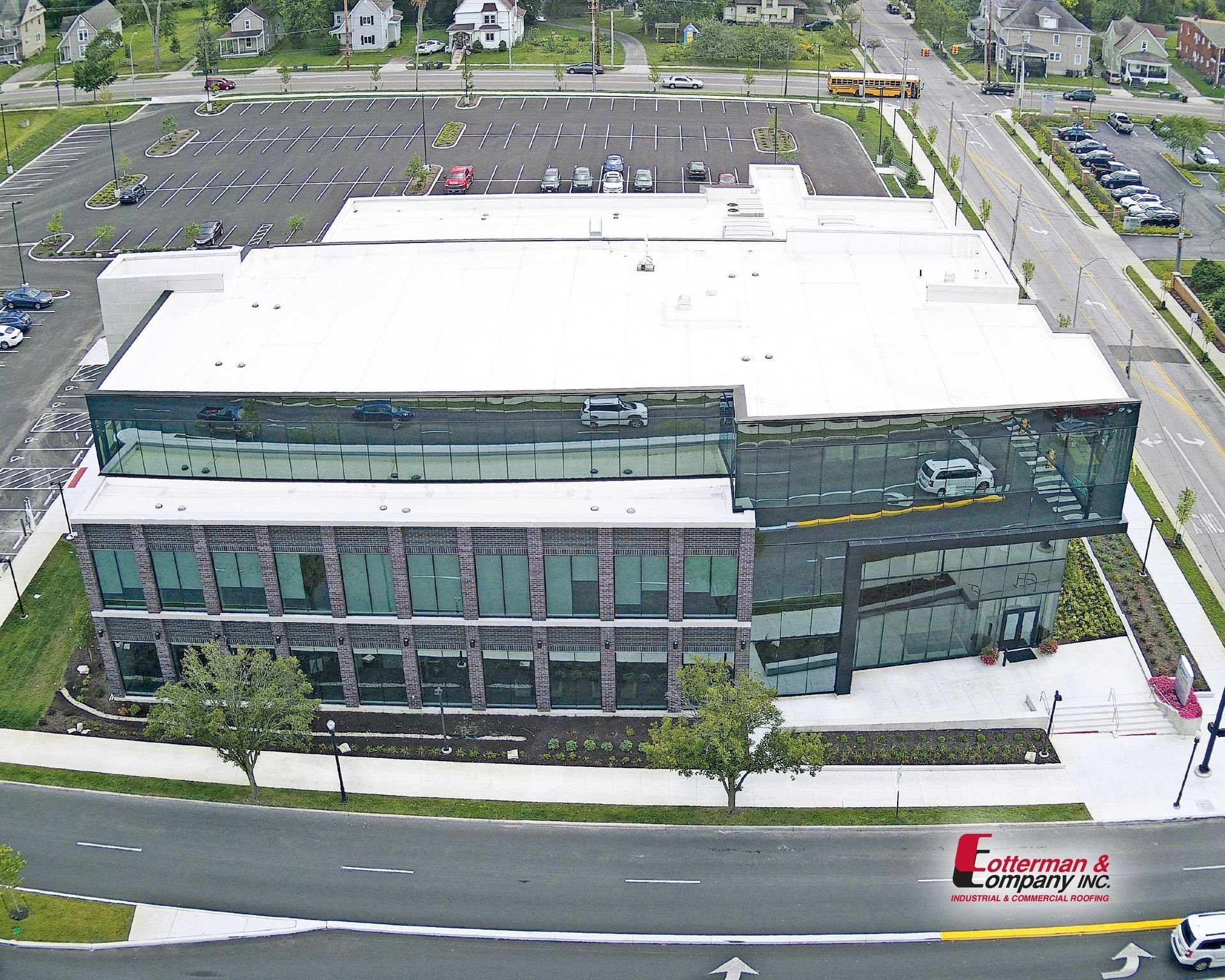 Modern building with glass and brick facade, large parking lot, and surrounding greenery.