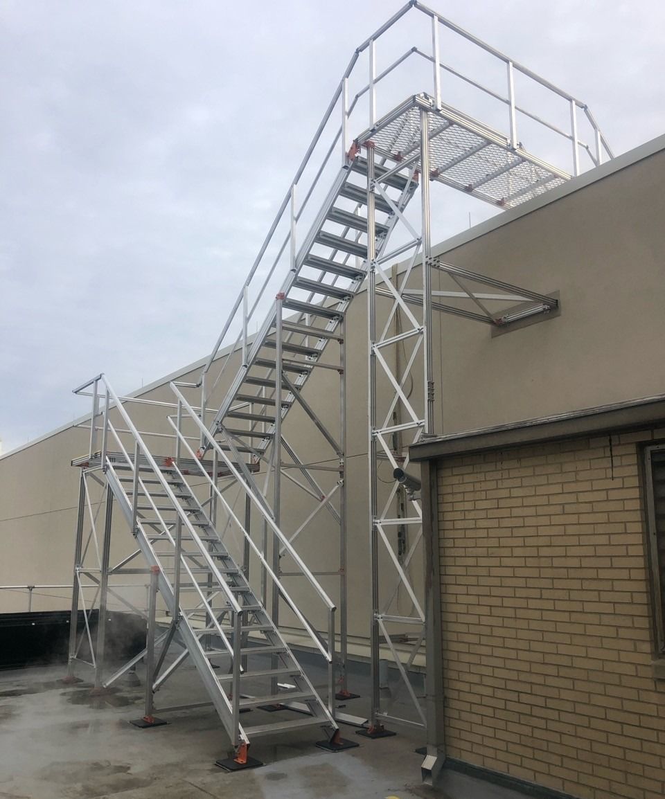 Exterior metal staircase leading to a rooftop platform on a tan building, under a cloudy sky.