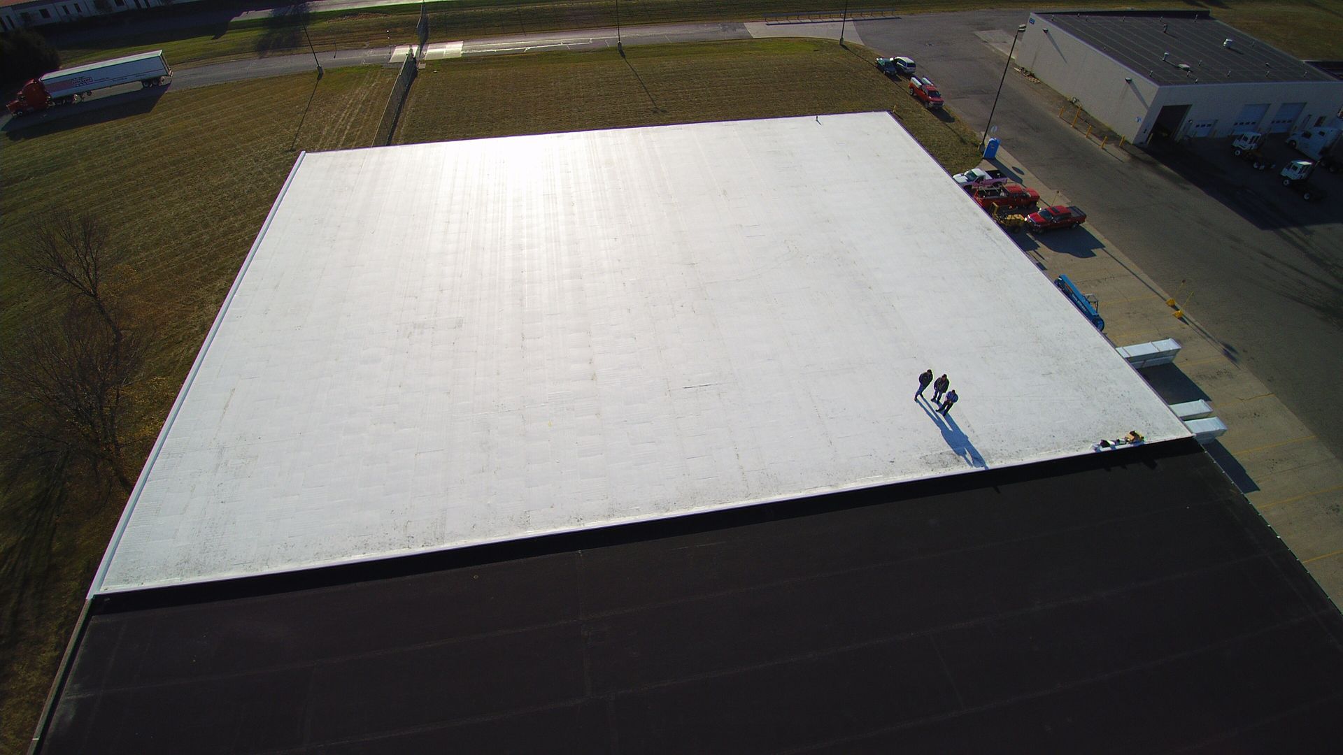 Aerial view of a white commercial roof with three people standing on it, near a black roof section.