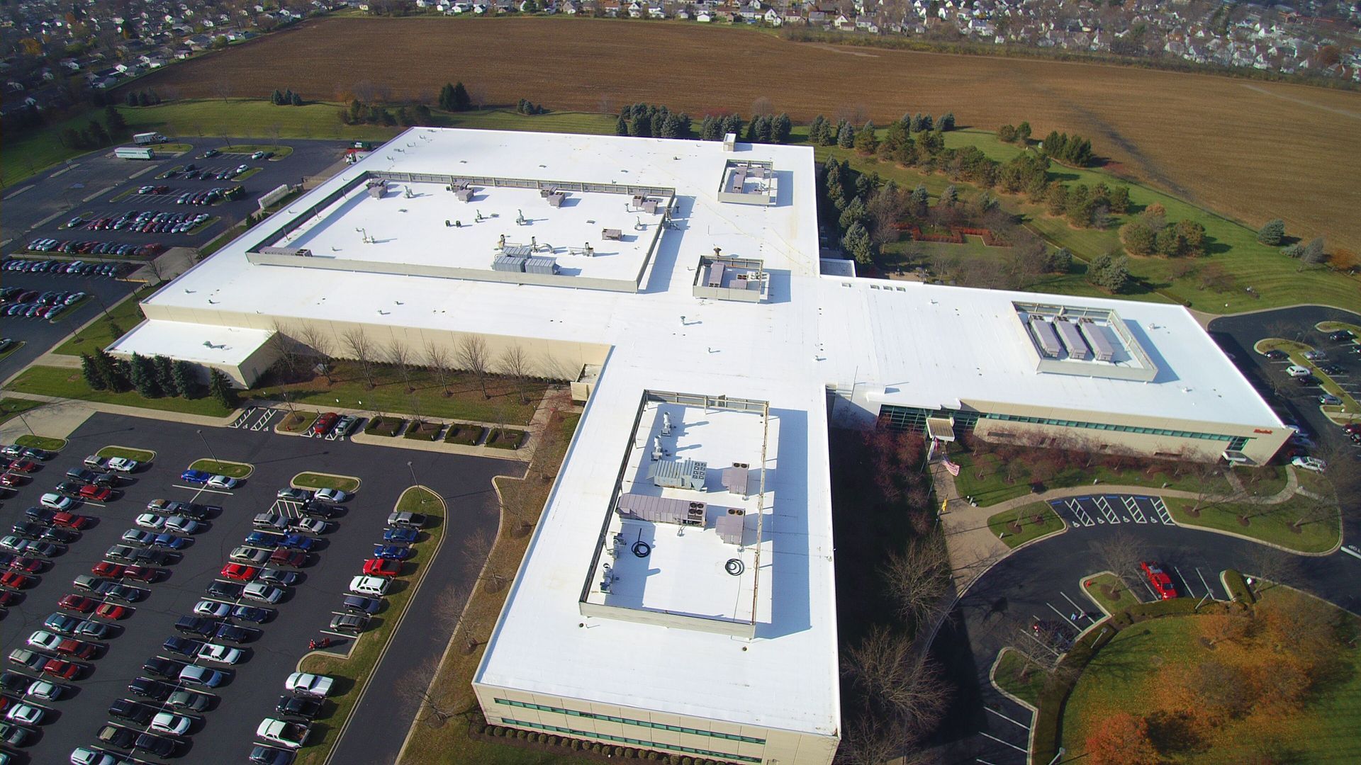 Aerial view of a large white commercial building with a sprawling roof and parking lot.