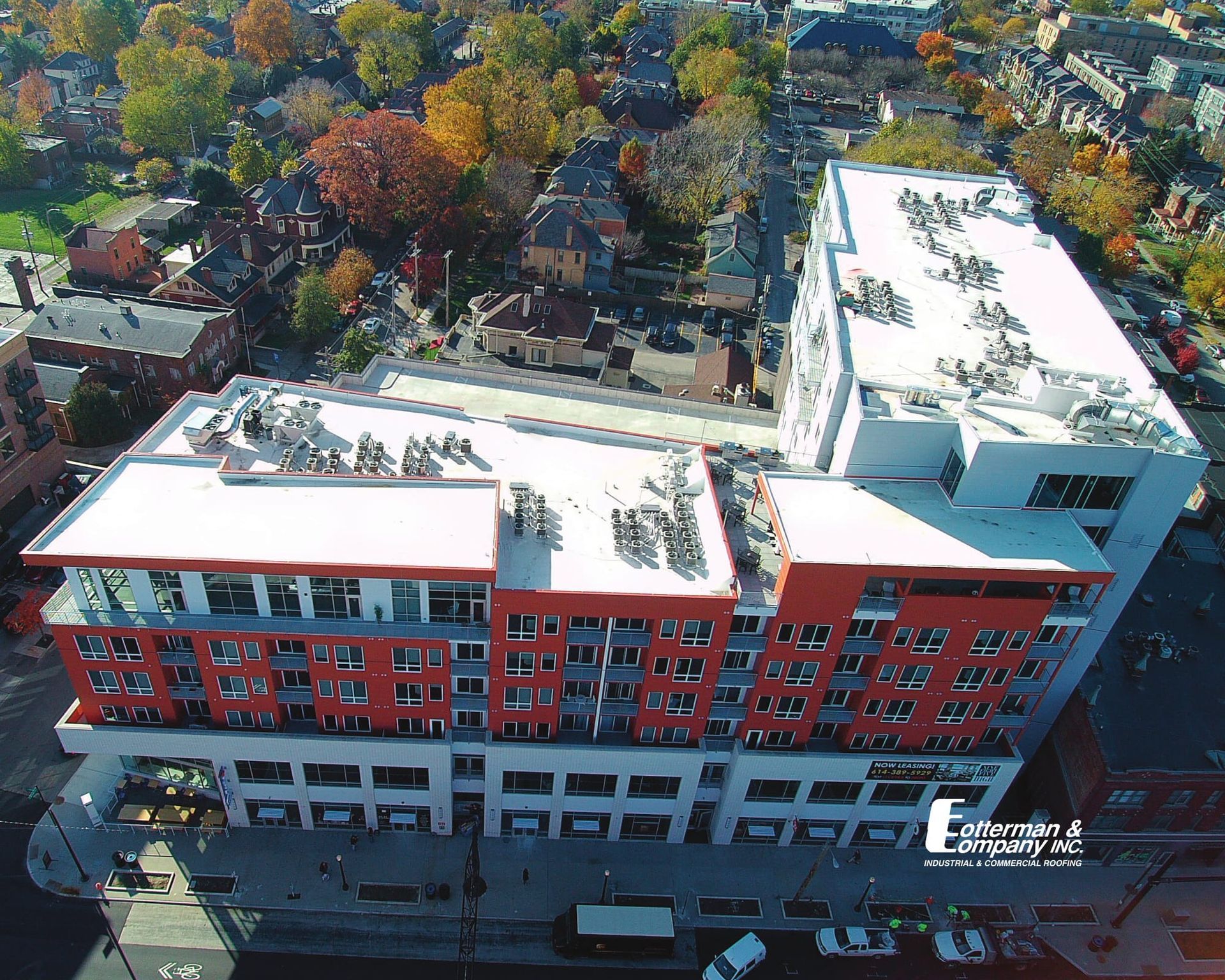 Aerial view of a modern multi-story building with a red and white facade, surrounded by trees and other buildings.