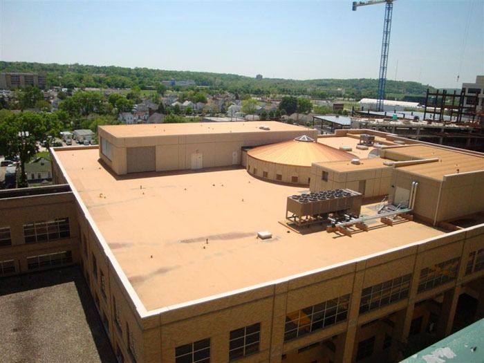 A view of a tan commercial building's flat roof with an air conditioning unit and a construction crane in the background.