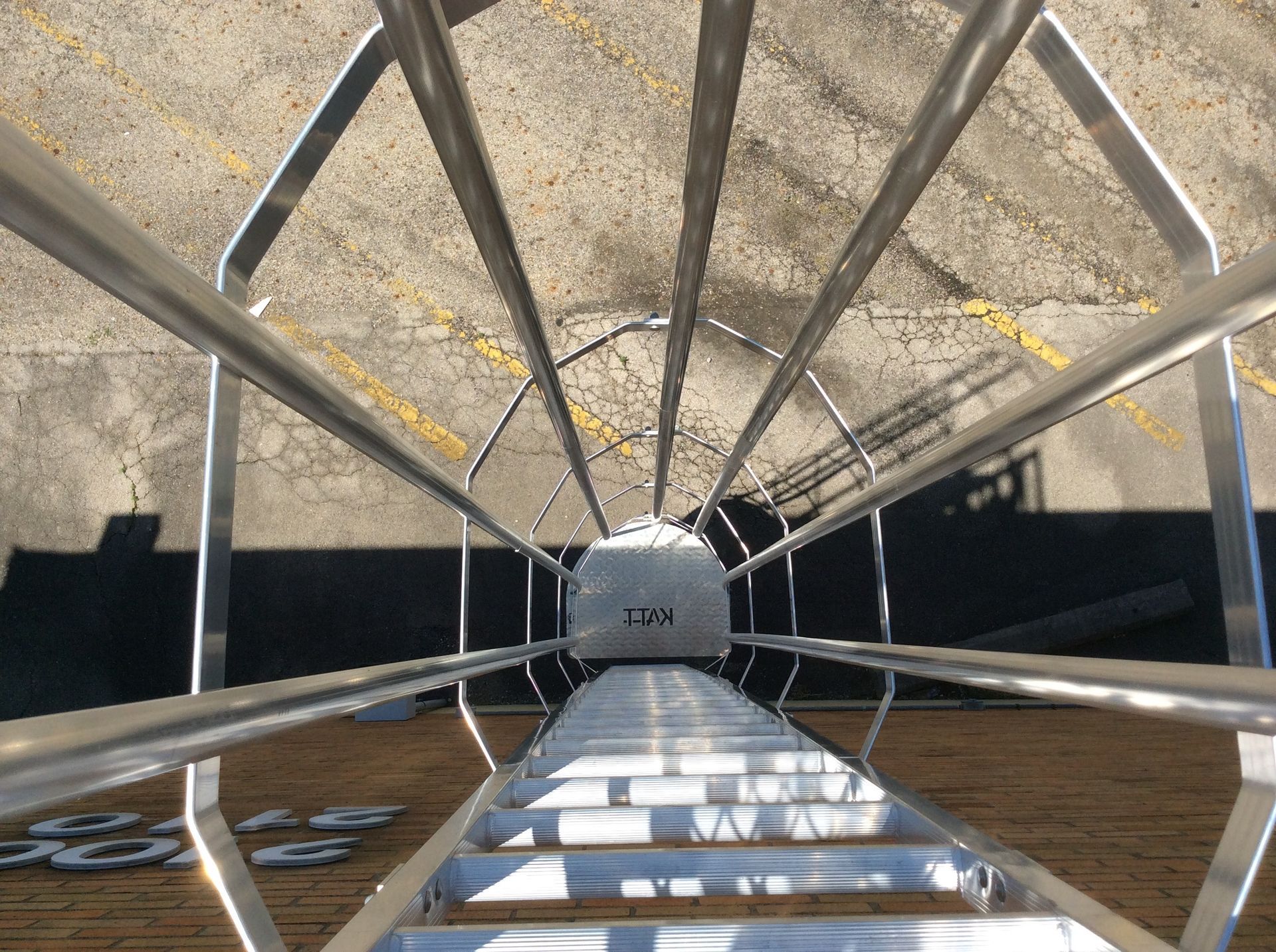 View from above of a ladder leading to a white cylindrical tank, surrounded by metal railings on concrete.