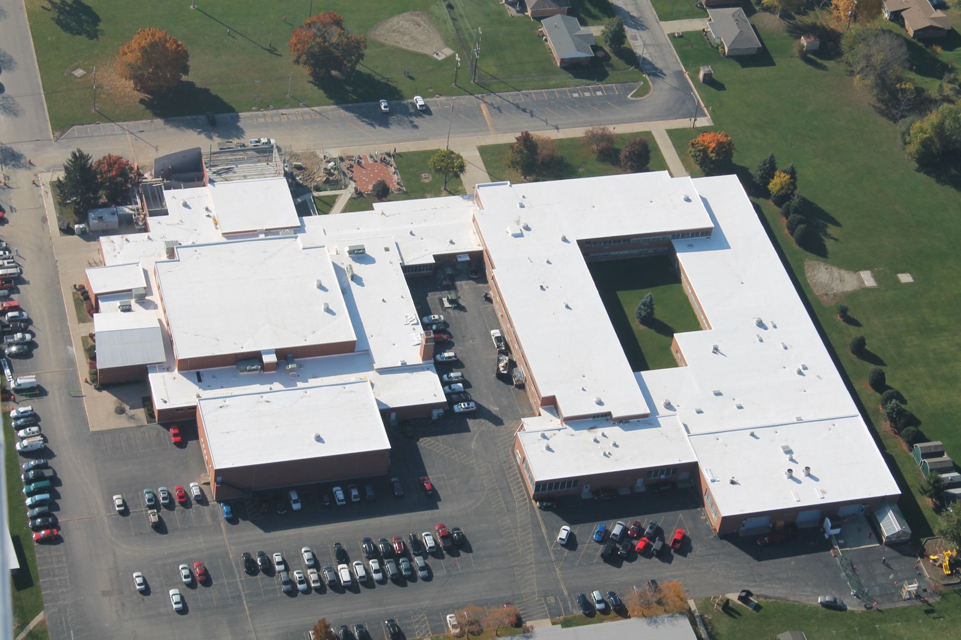 Aerial view of a school building with a white roof and multiple parking lots filled with cars.