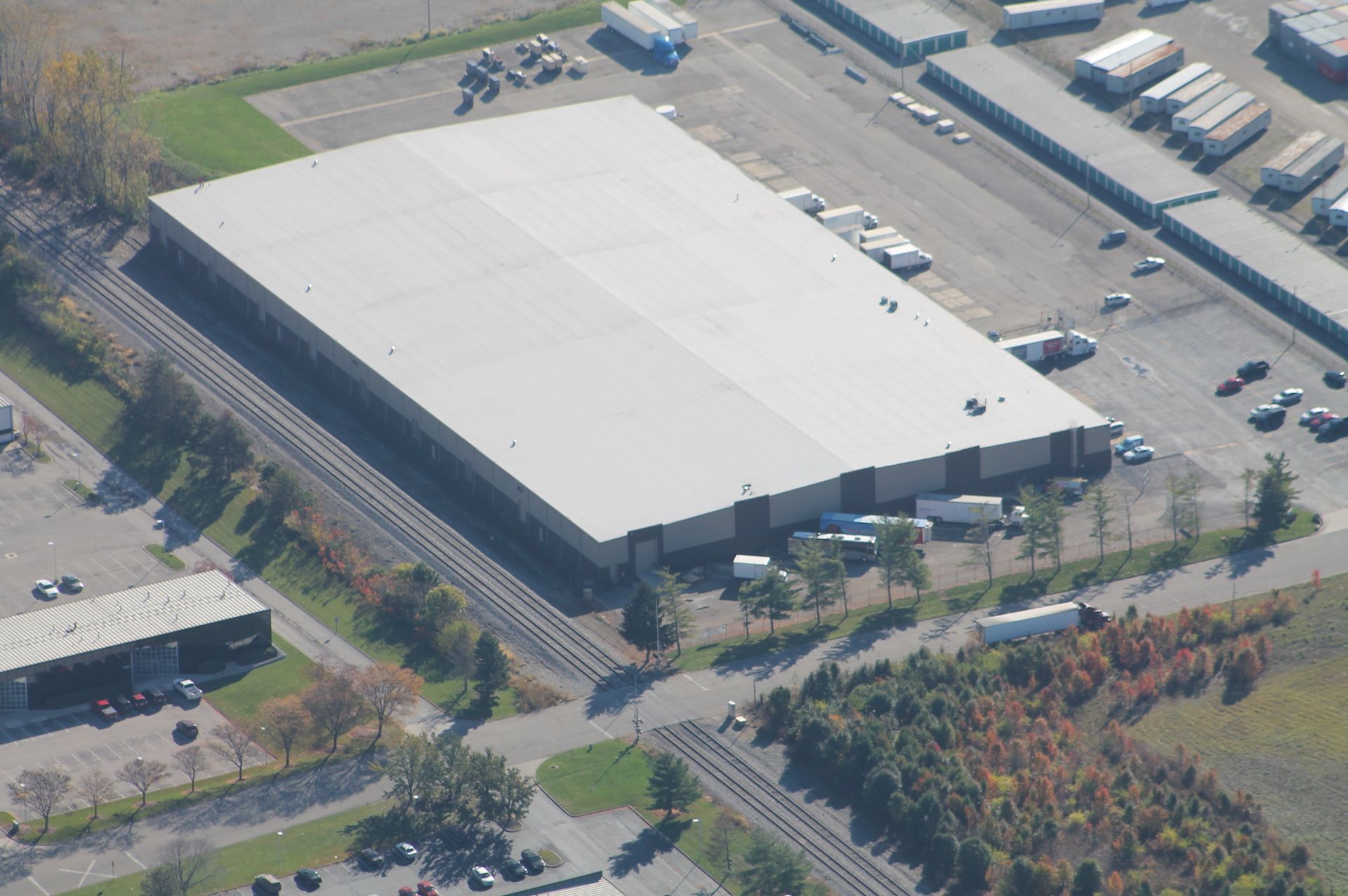 Aerial view of a large industrial warehouse building with rail tracks alongside and trucks parked at loading docks.