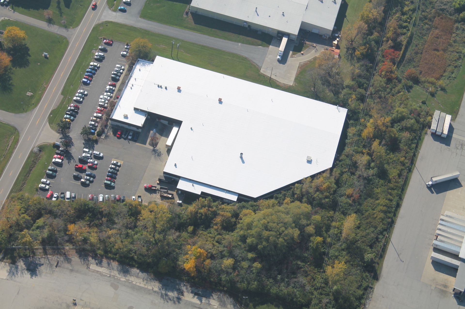 Aerial view of a white commercial building with a large parking lot and surrounding trees.