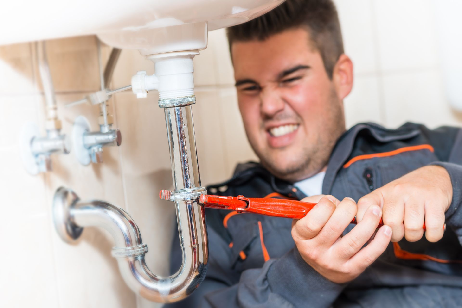 A plumber is fixing a sink with a wrench.
