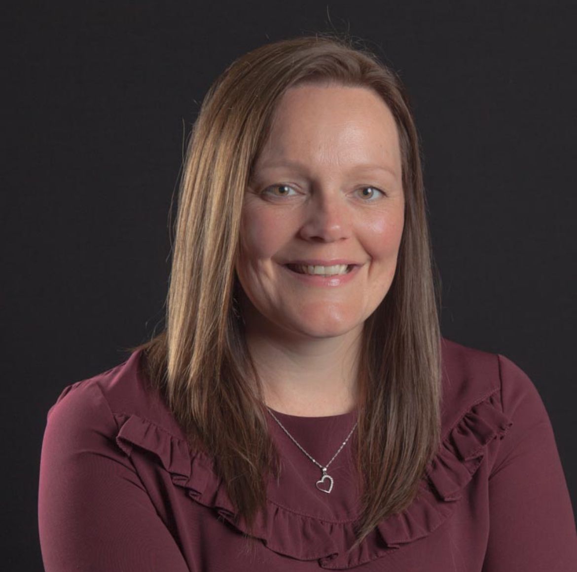 A woman wearing a maroon shirt and a necklace is smiling for the camera.