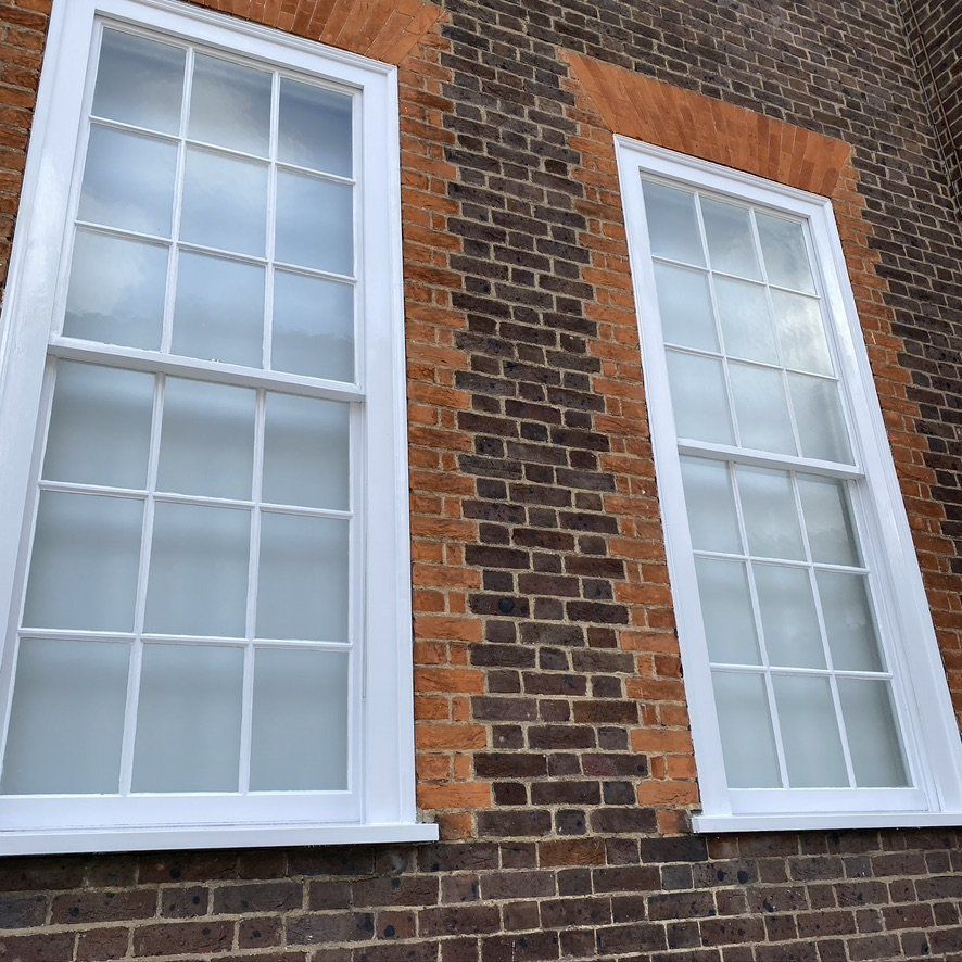 Two white-framed, multi-pane windows on a red-brick building.