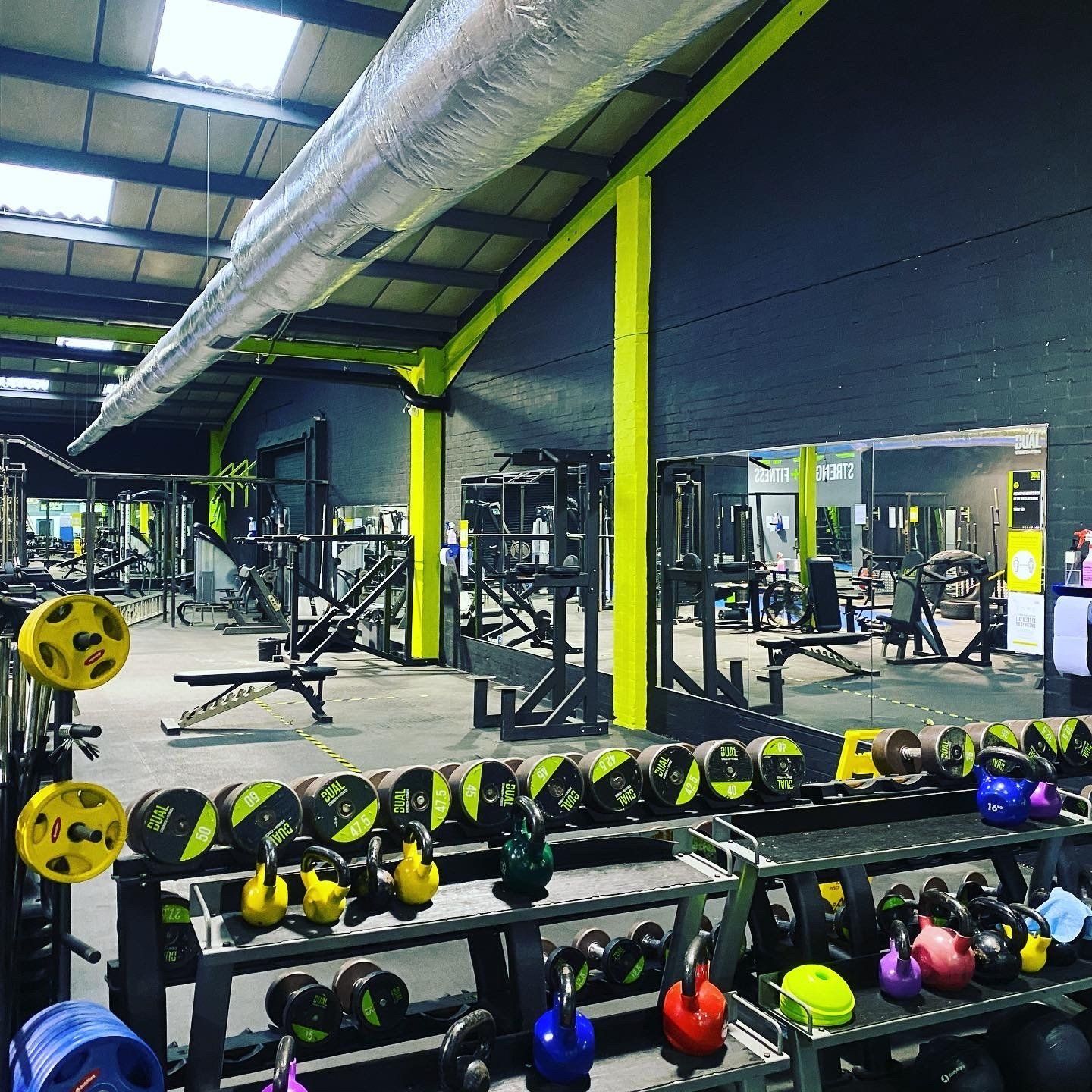 Gym interior with weight machines, free weights, and colorful kettlebells.