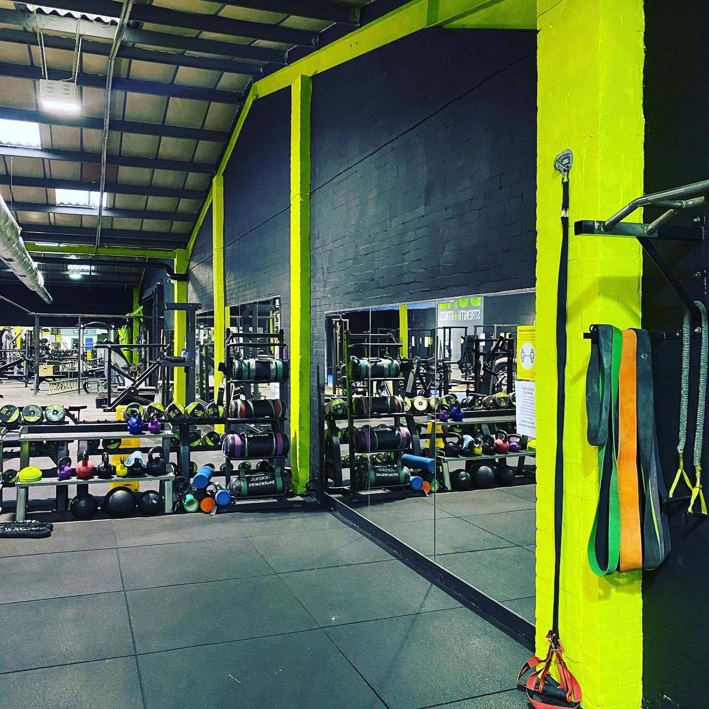 Gym interior with fitness equipment. Gray floor, yellow and black walls, various weights, and exercise machines.
