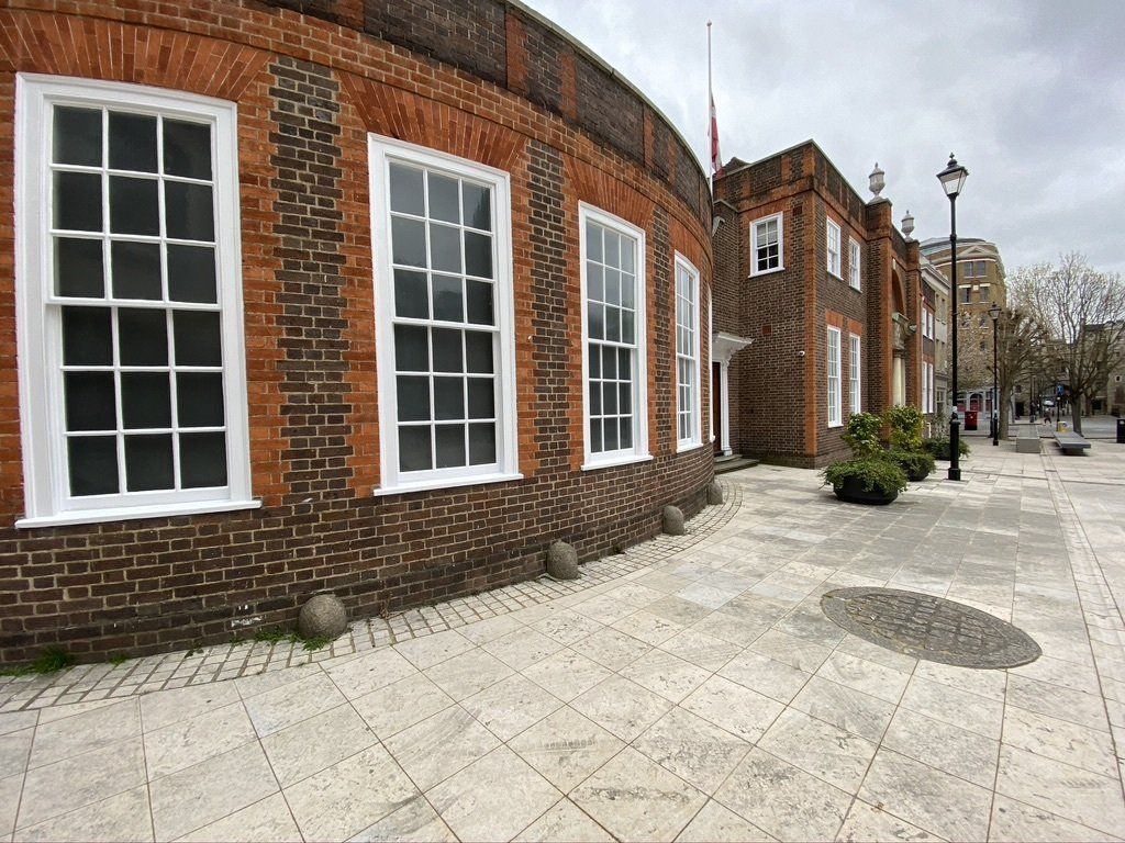 Brick building with large white-framed windows, paved walkway in front.