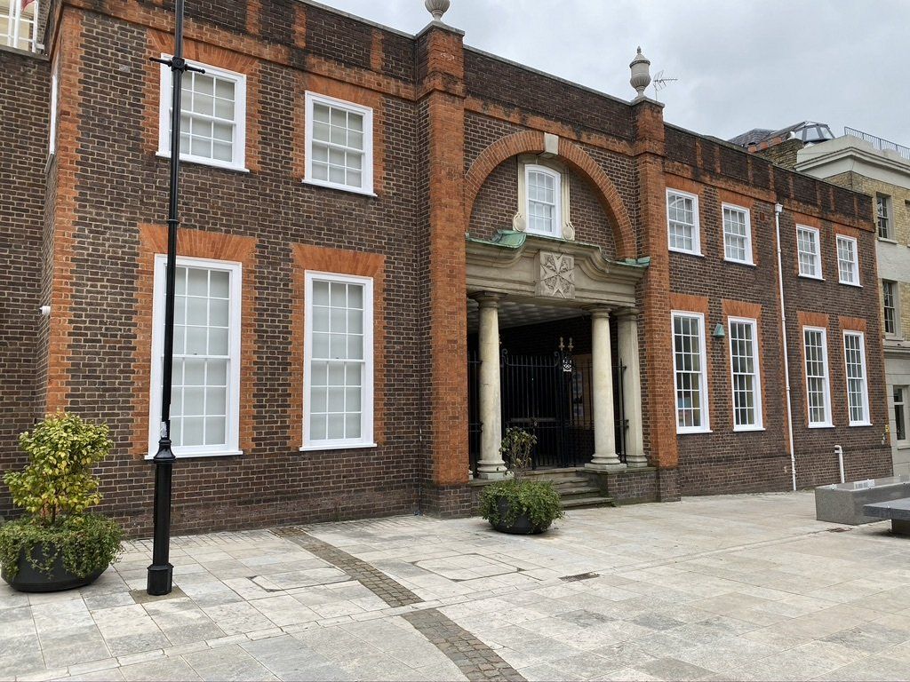 Brick building with white windows, arched entrance, and a paved courtyard.