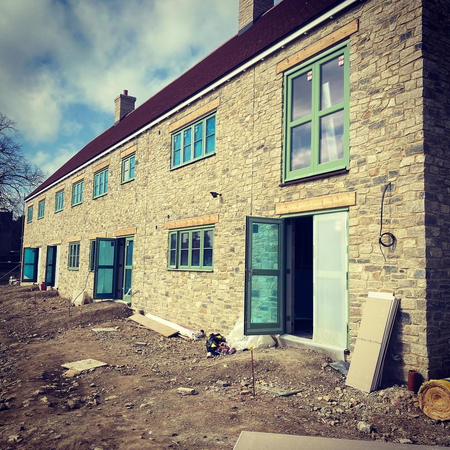 Row of stone buildings under construction with green window frames and doors.