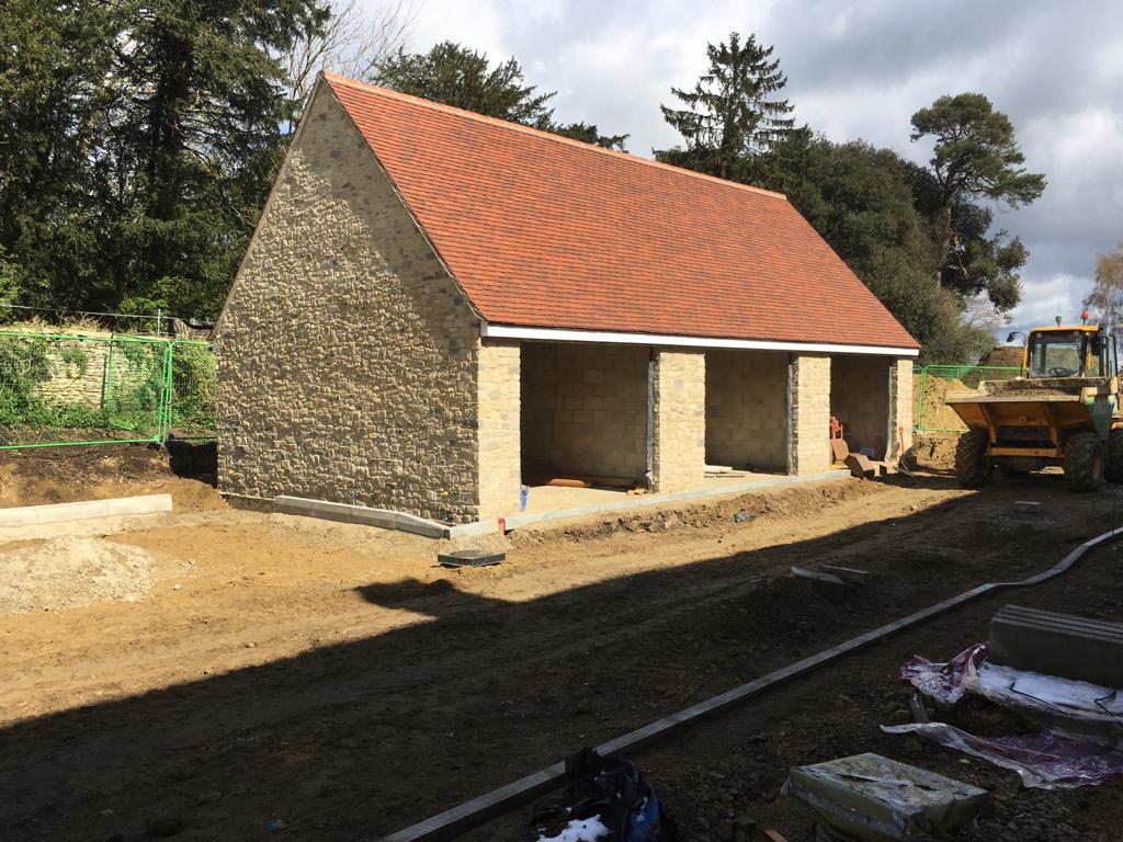 Stone building under construction with a red tile roof and three open bays; a yellow tractor is visible.