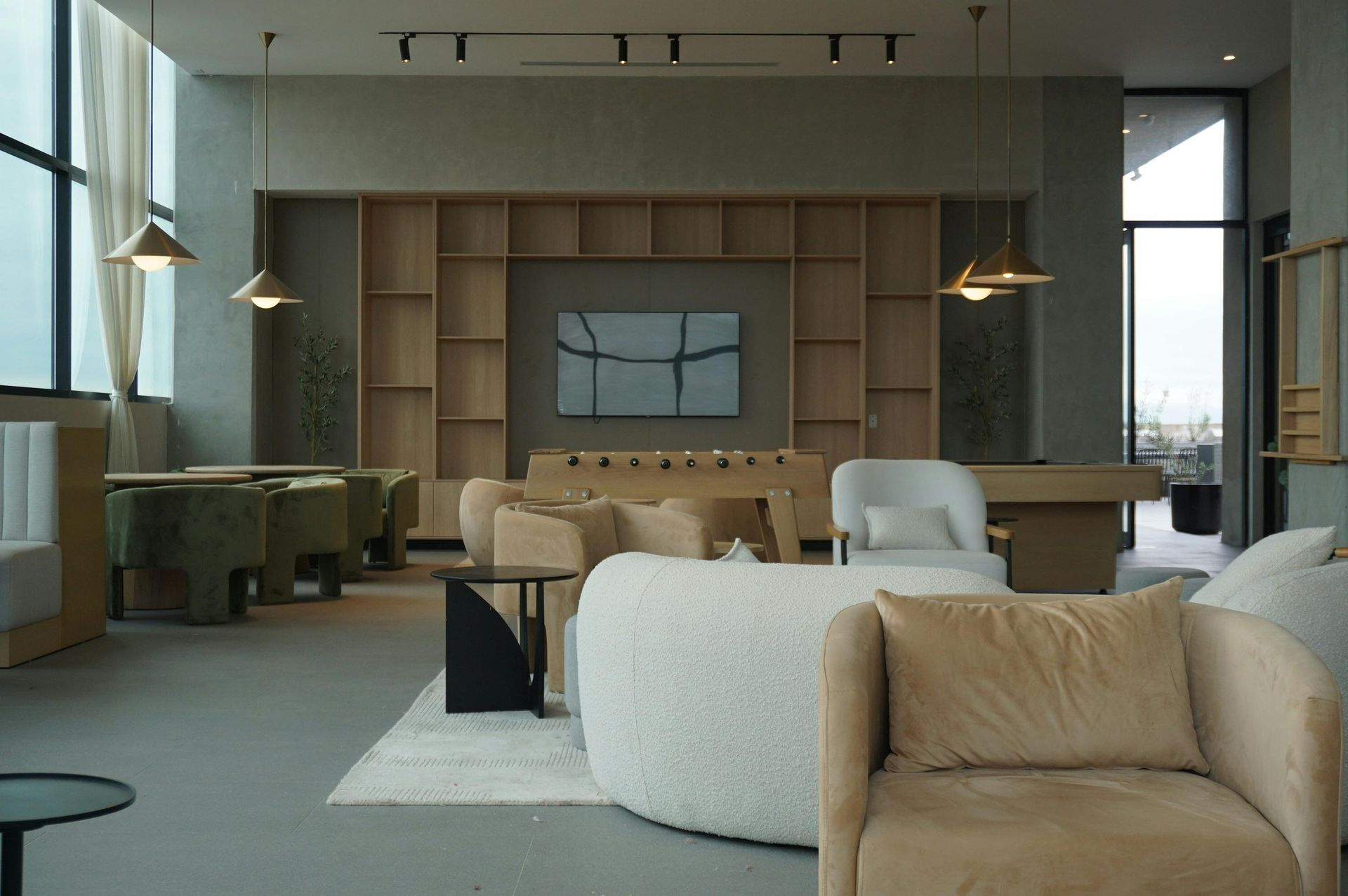 Modern lounge area with neutral tones, shelves, armchairs, and foosball table.
