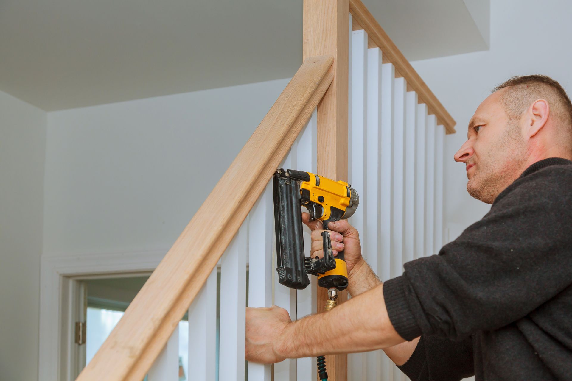 A builder installing a railing for stairs with an air gun.