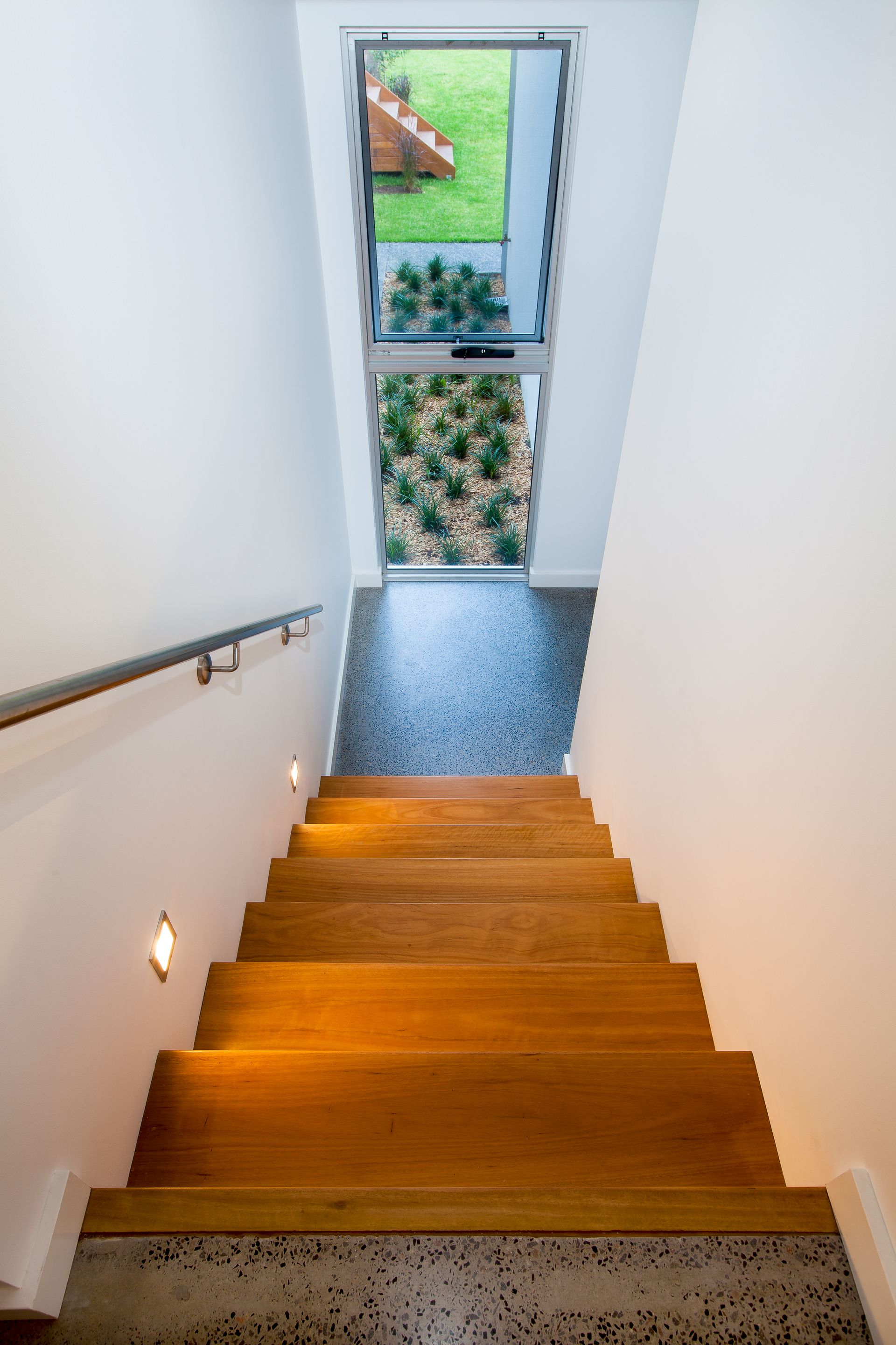 Wooden staircase leading up to a doorway with a view of a grassy yard. White walls, handrail.