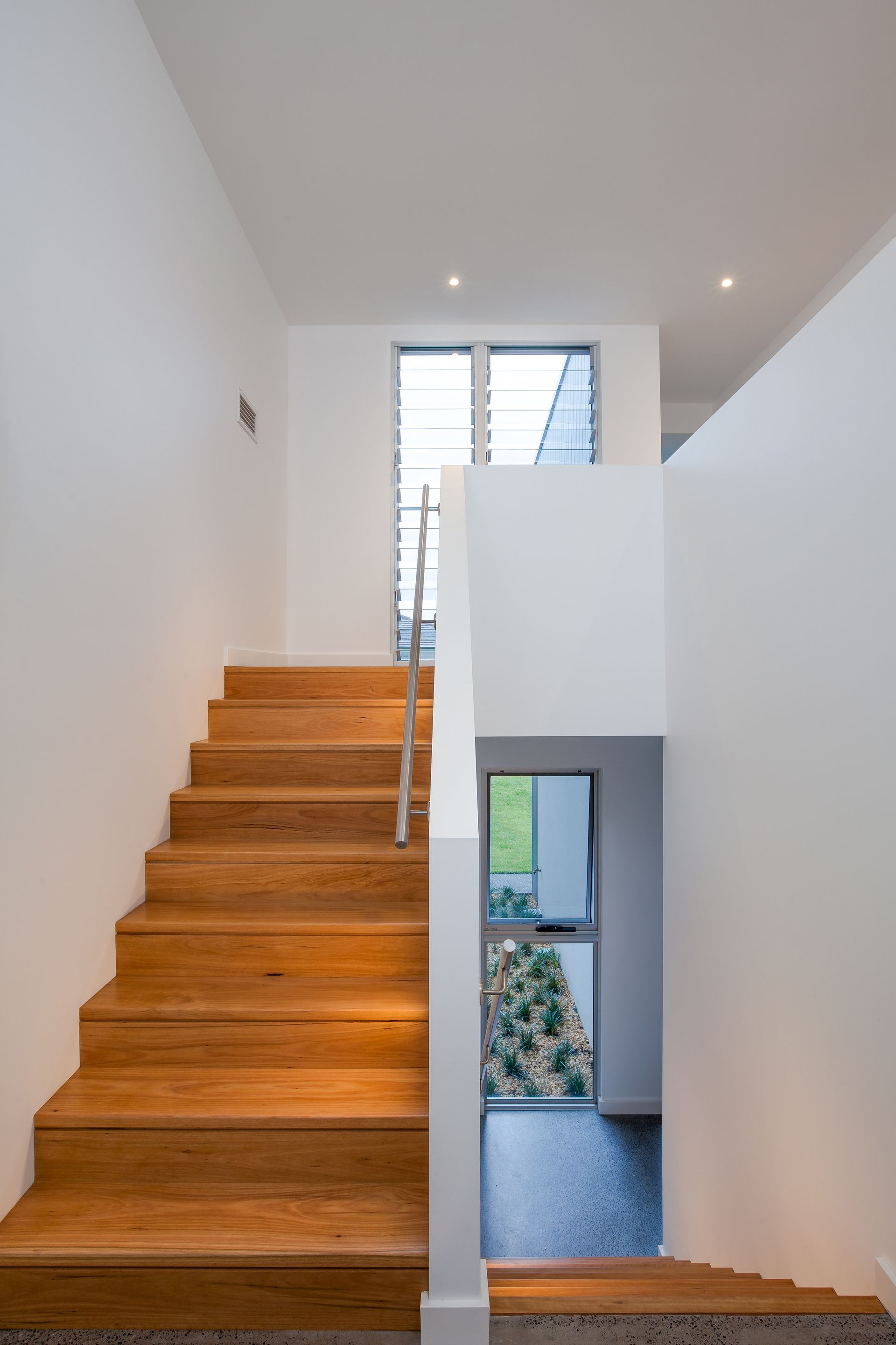 Wooden staircase with white walls, windows visible at the top, natural light.