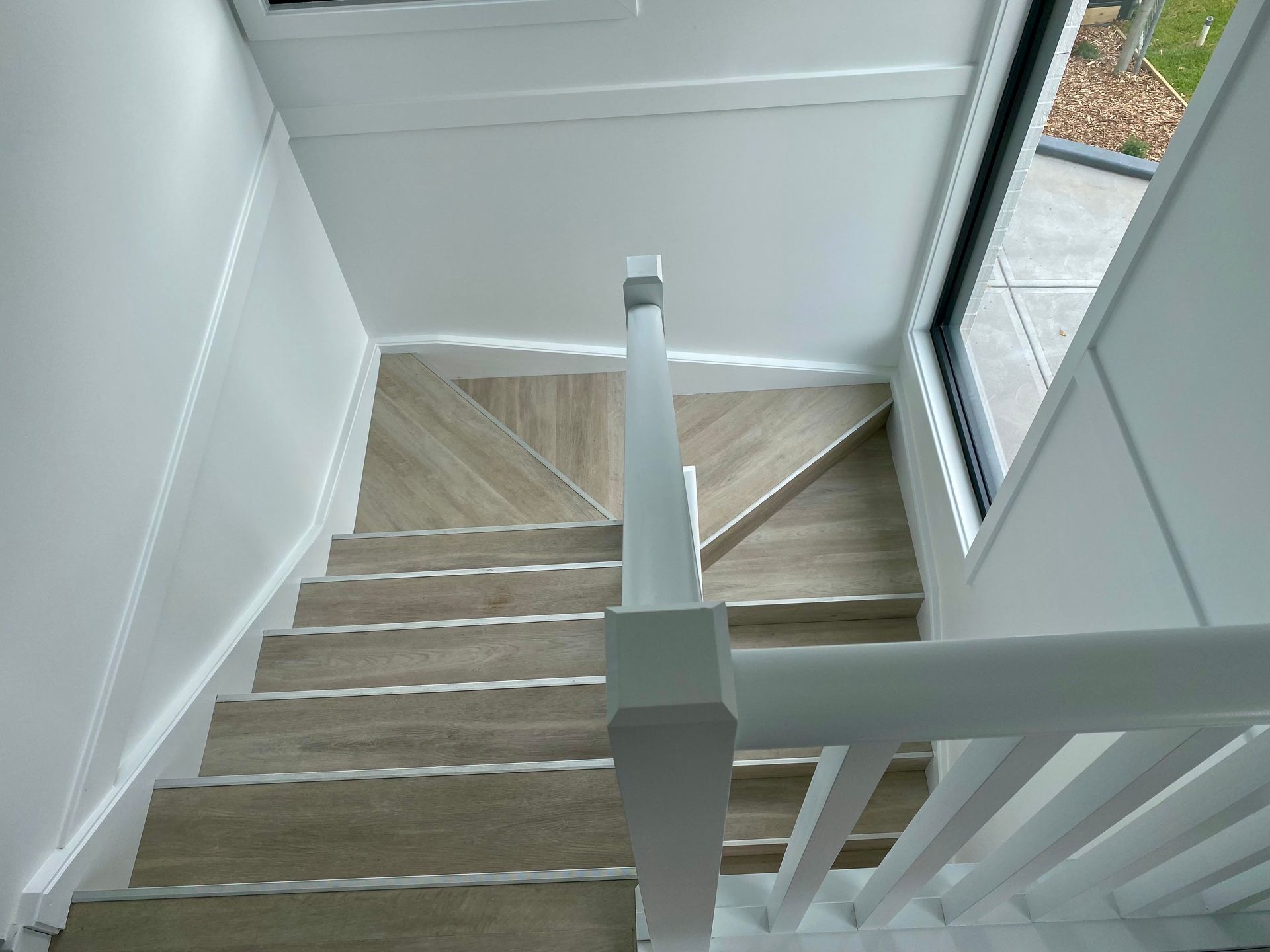 Staircase with light wood treads and white banister, viewed from above.