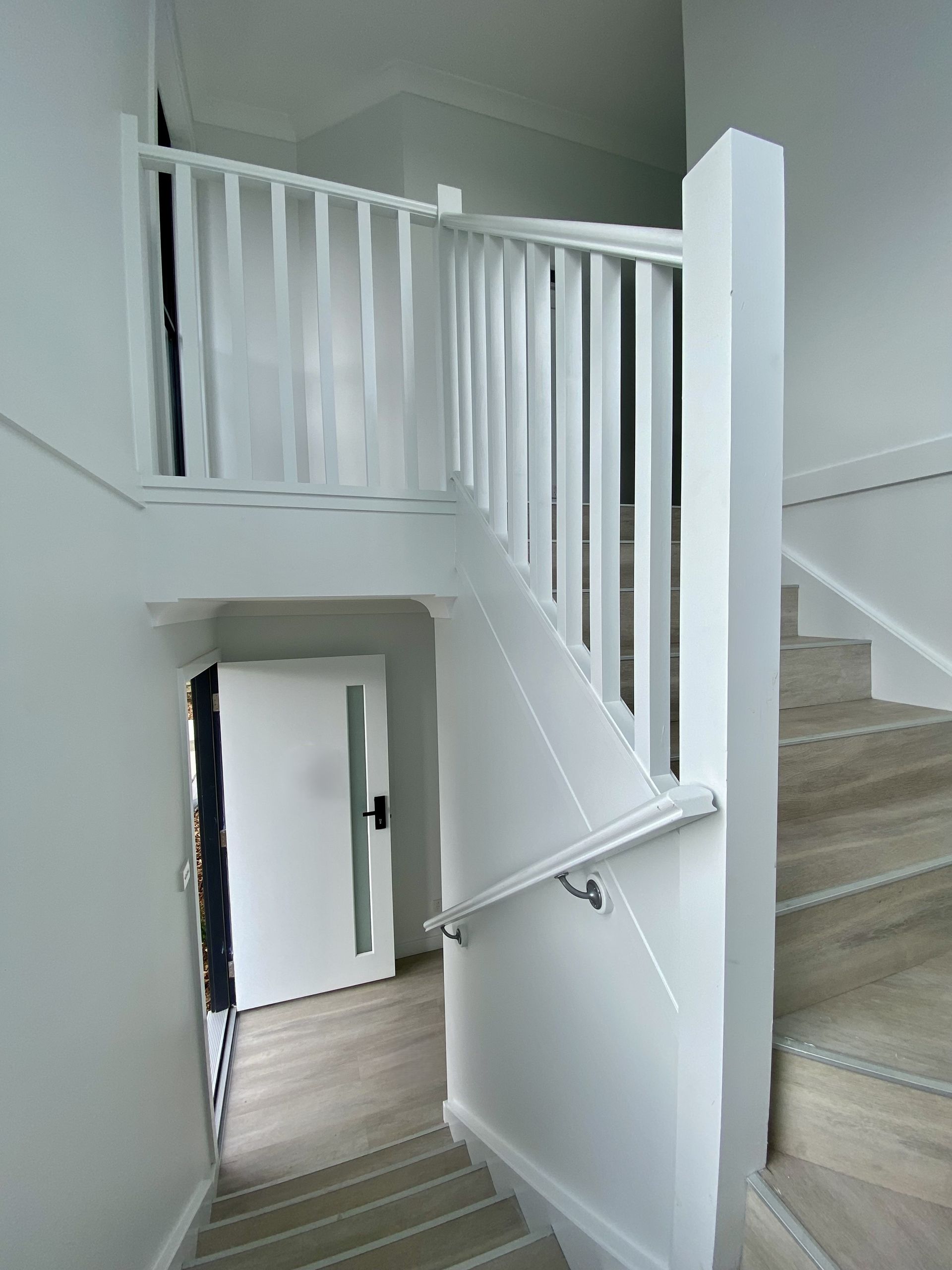 White staircase with railing and handrail, leading down to a door.