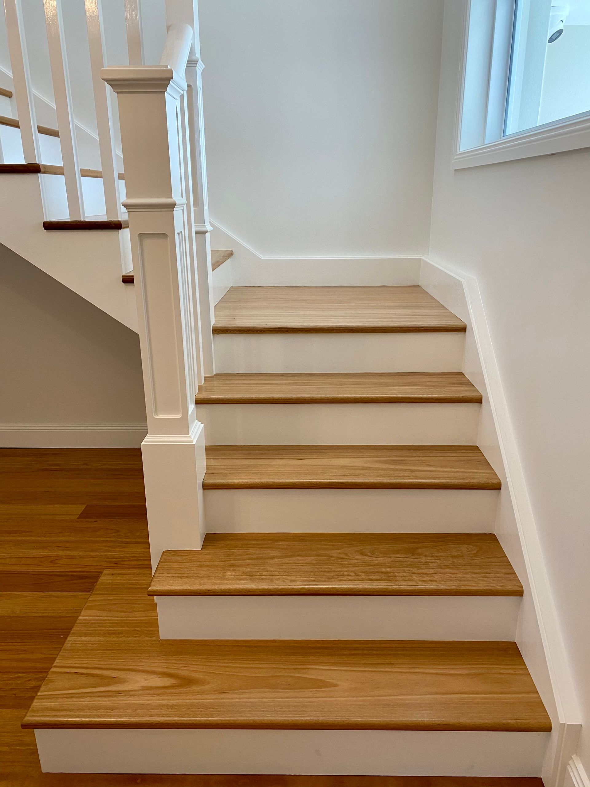 Wooden staircase with white trim, leading upwards against a white wall.