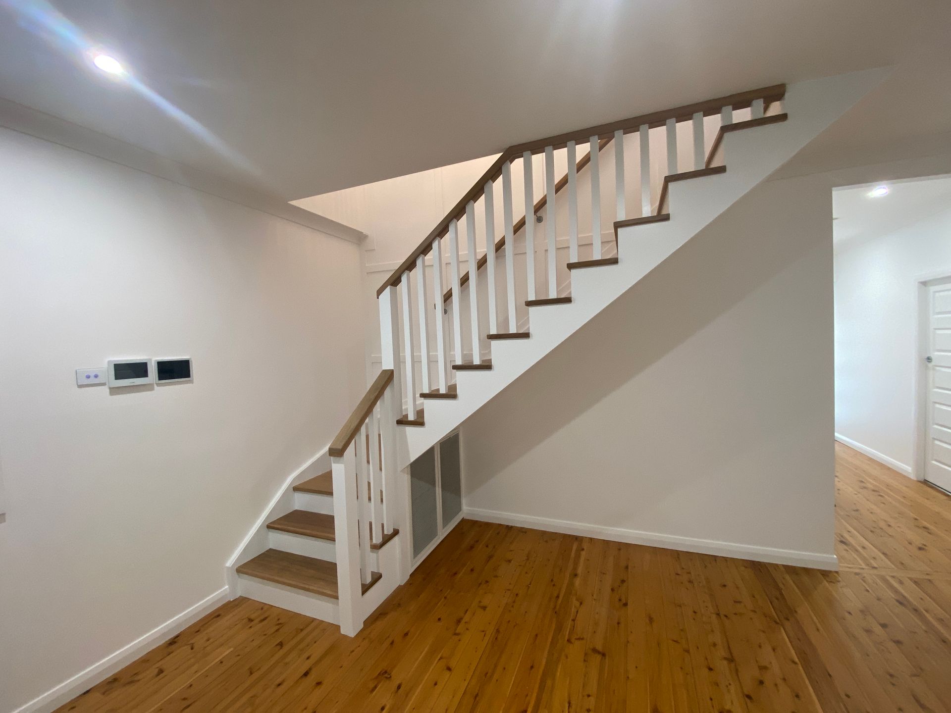 Staircase with white balusters and brown handrail. Wooden steps and floor, white walls.