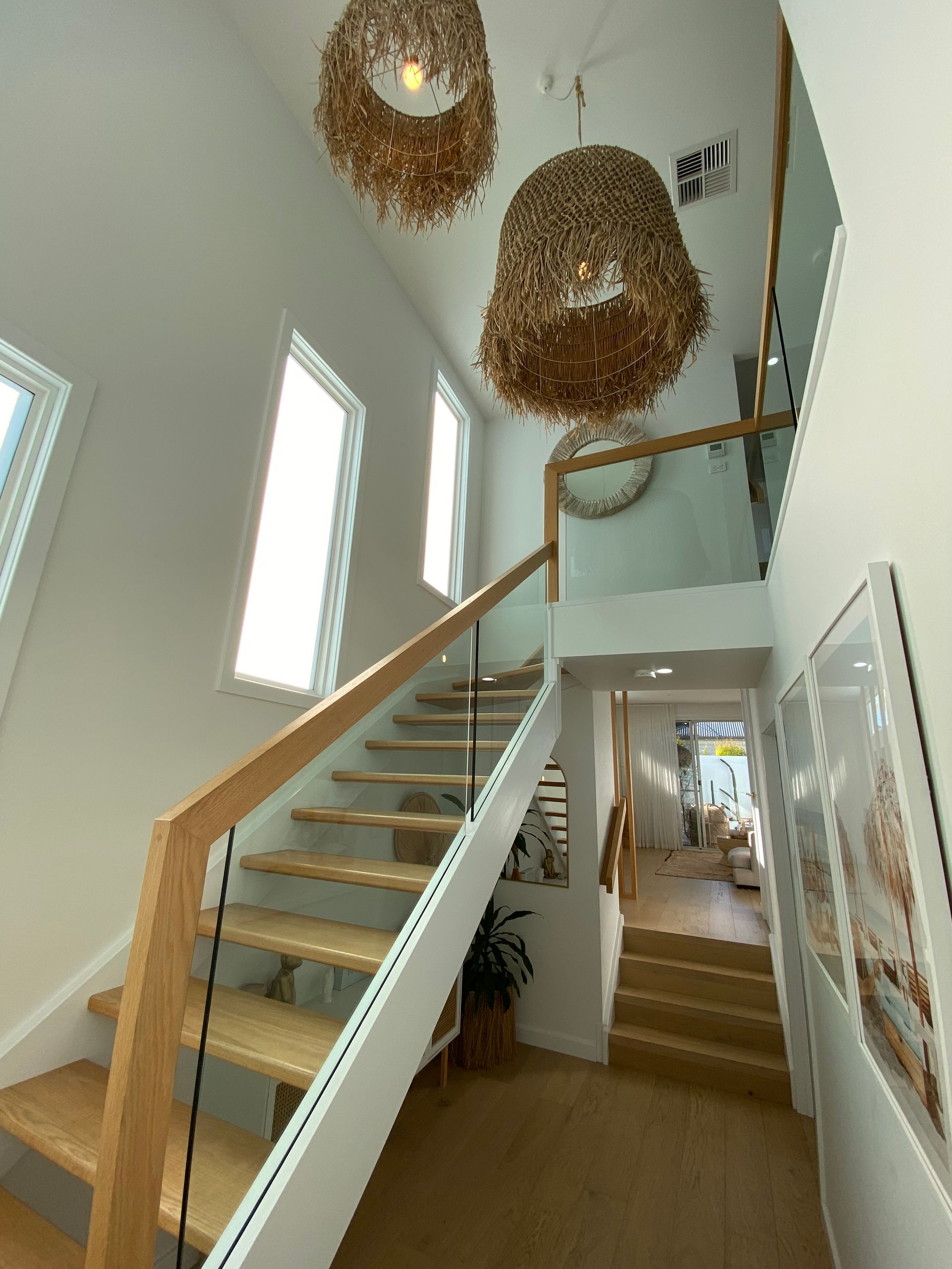 Bright staircase with wooden steps and glass railing, leading to a light-filled hallway with pendant lights.
