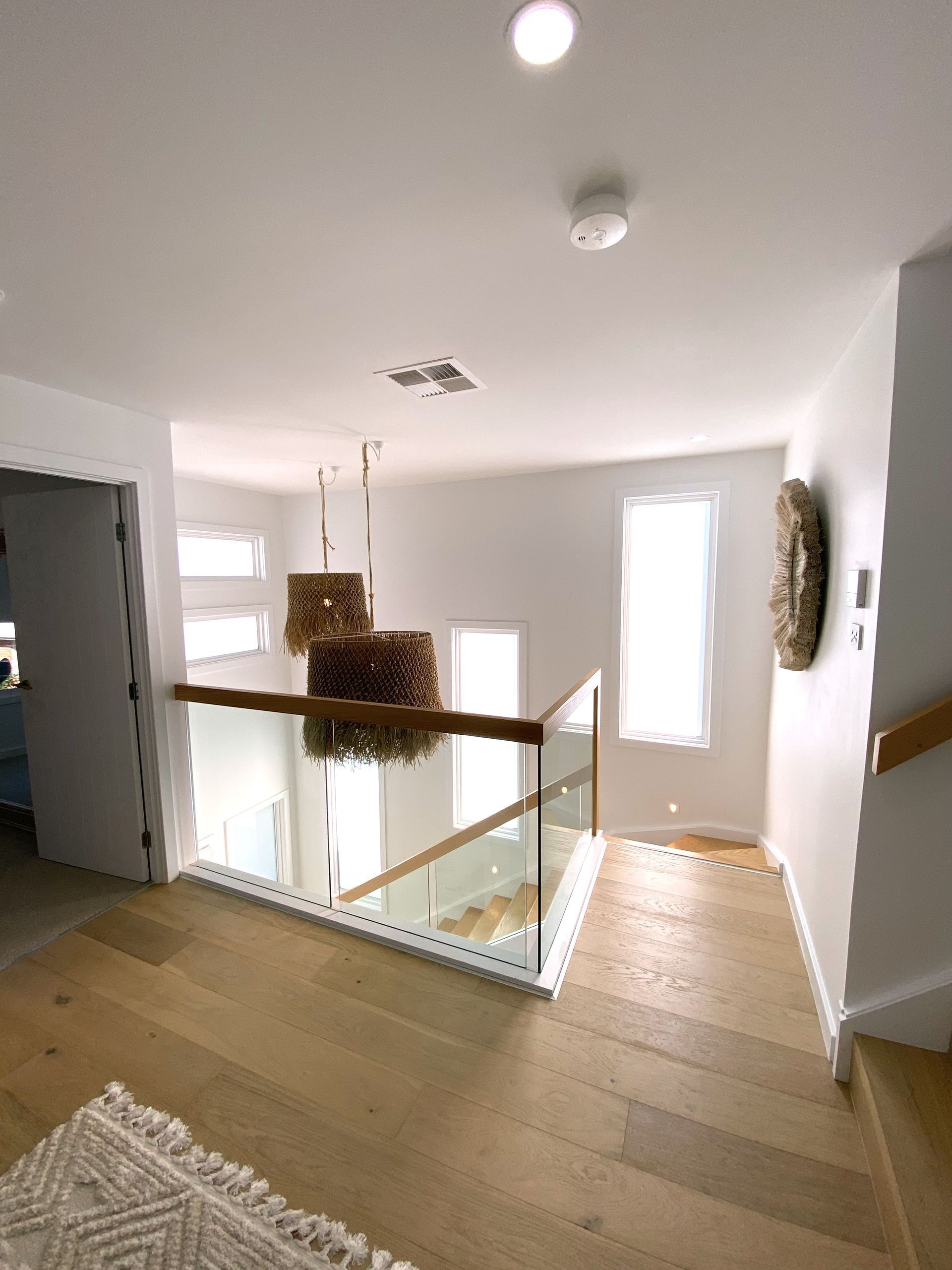 Hallway with wooden floor, glass railing, white walls, and pendant lights.