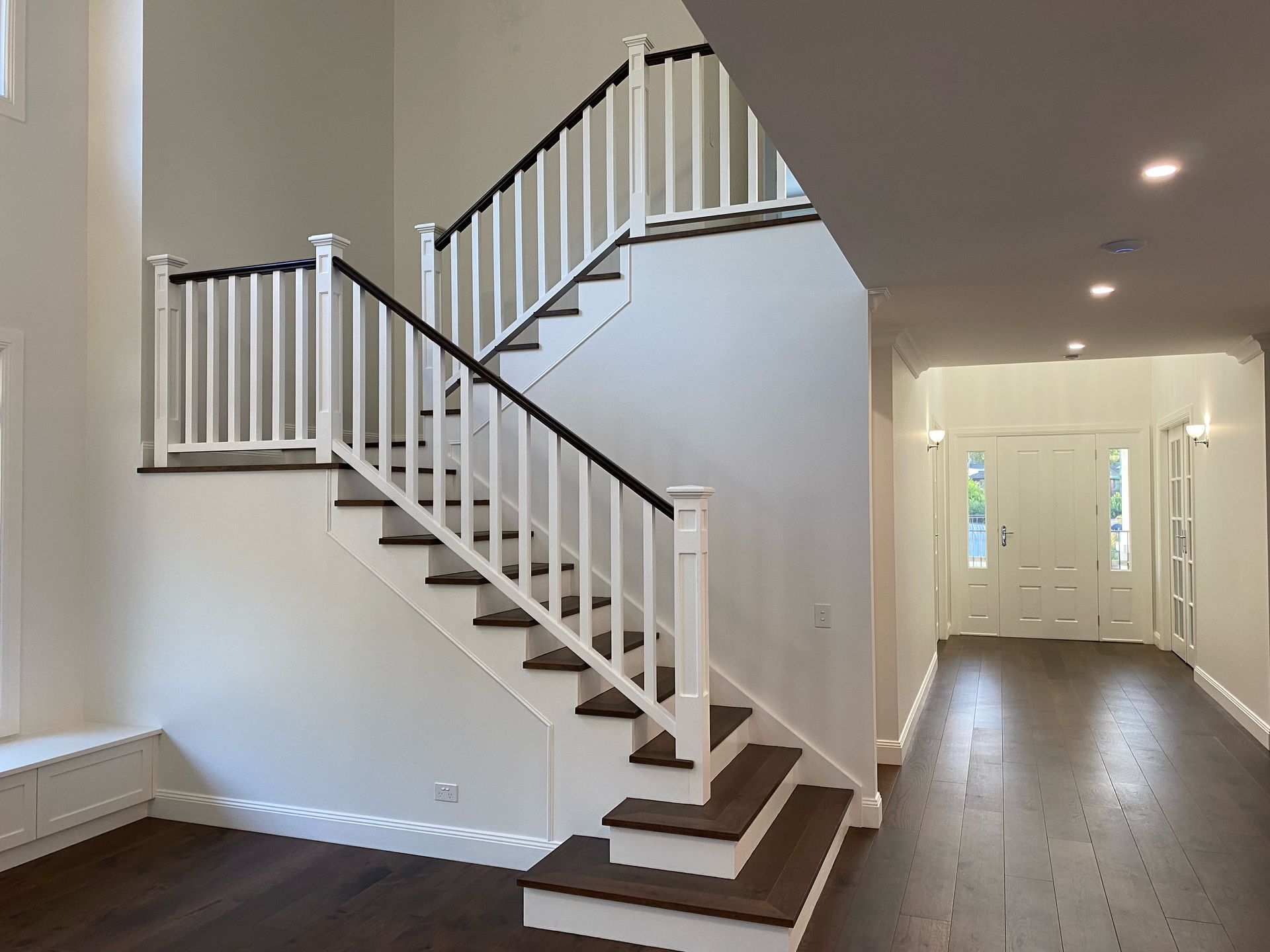 Interior view: staircase with white balusters, dark wood steps, hallway with front door, and dark wood flooring.
