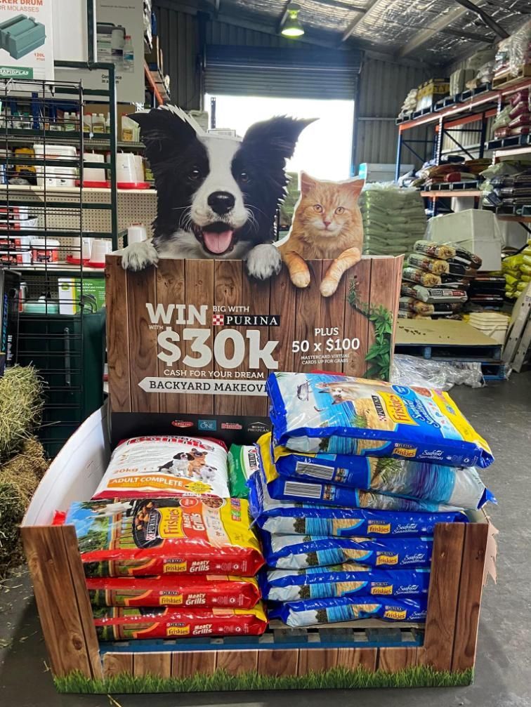 Dog and cat display above stacked pet food bags, inside a store, promoting a $30k giveaway.