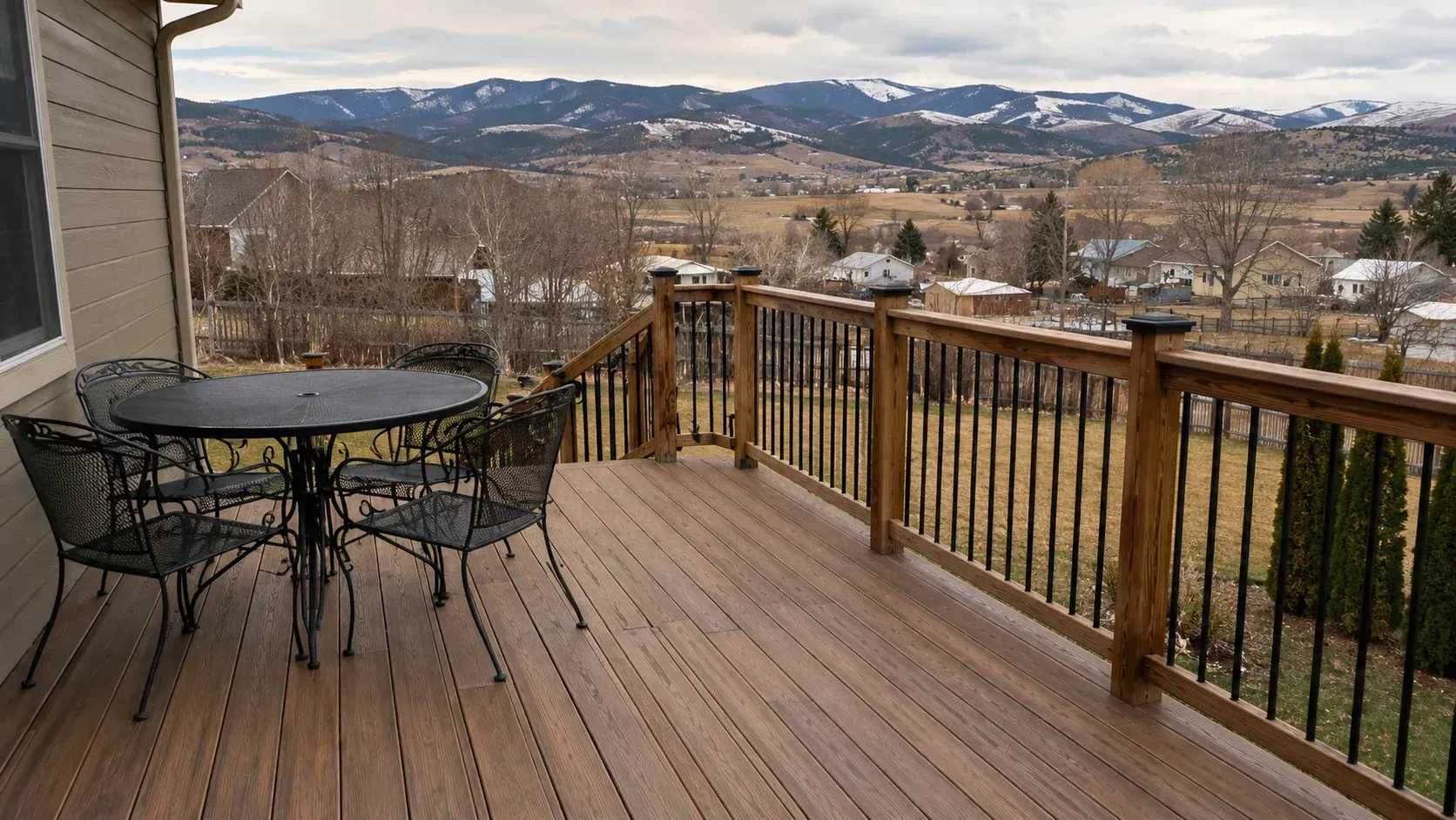 A wooden deck with patio furniture and railings overlooking scenic Montana hills, showcasing what's the best decking material for Montana's climate.