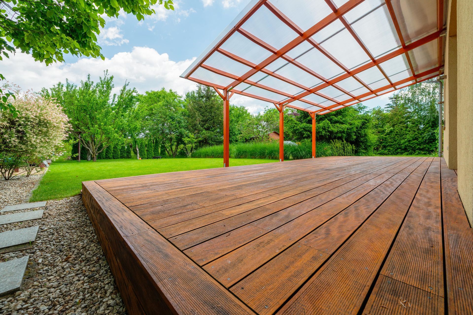 Wooden deck beside a grassy yard under a red-framed translucent pergola