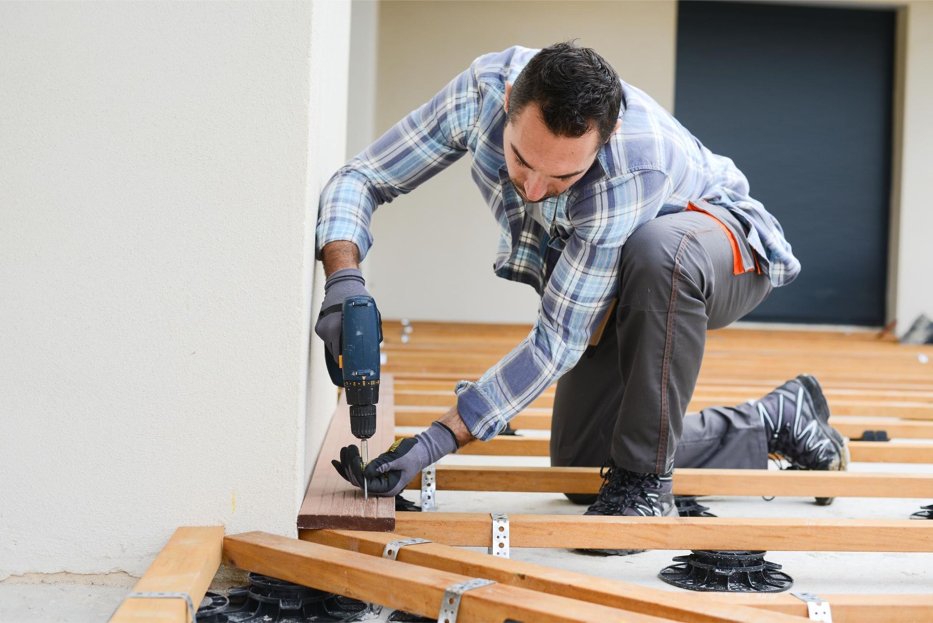 Worker using a power drill to fasten wooden floor framing indoors