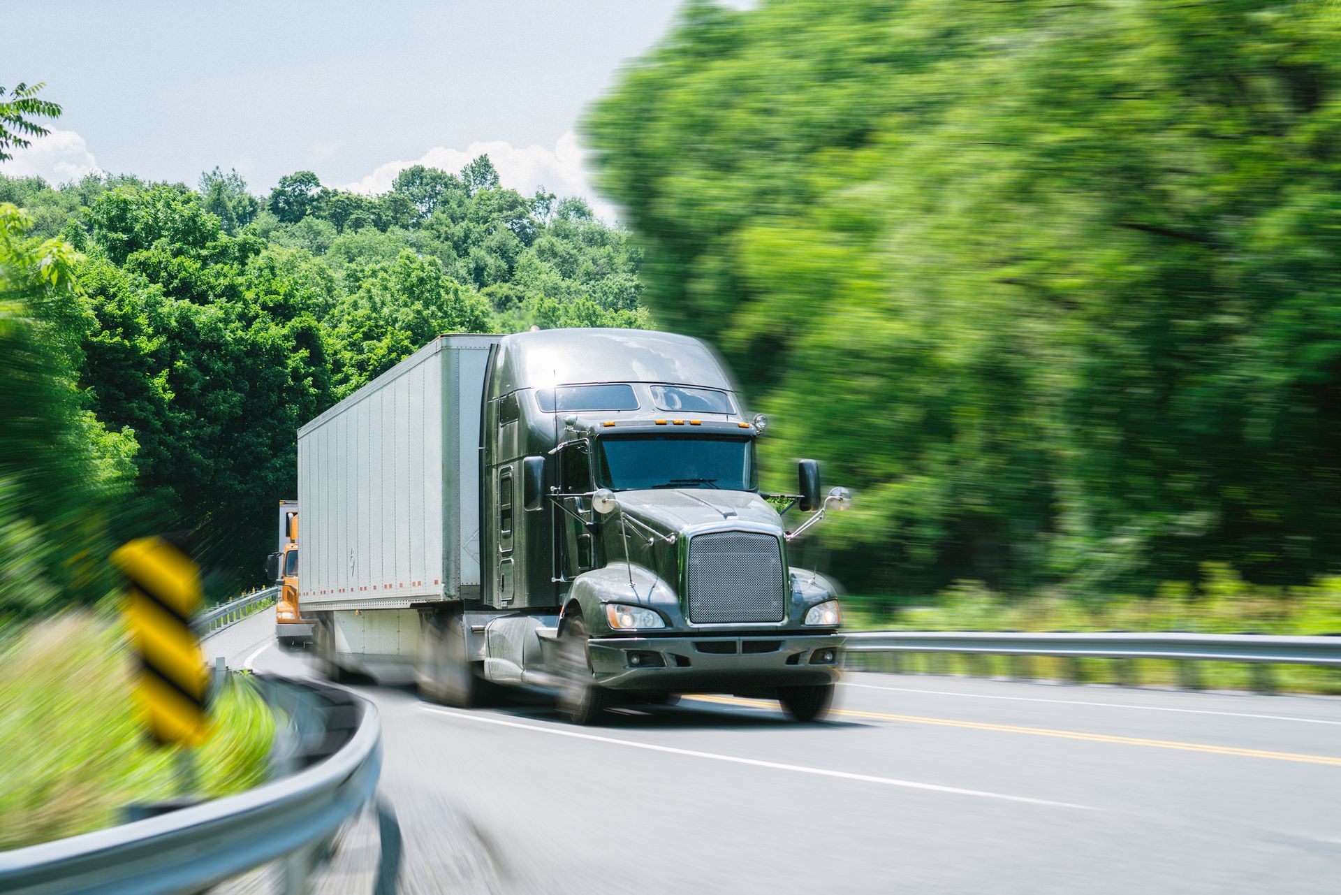 A semi truck is driving down a highway next to trees. A semi truck is driving down a highway next to trees.